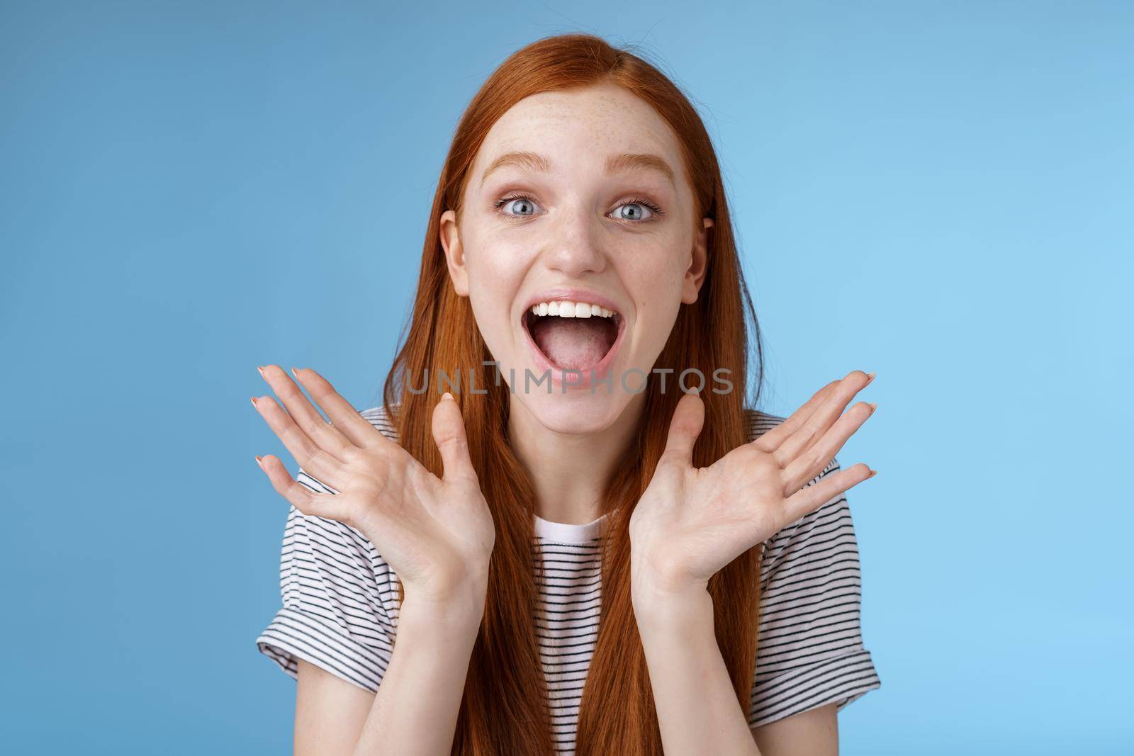 Happy cheerful rejoicing young pretty redhead supportive girlfriend clasp hands joyfully yelling congratulations raising hands amused wide eyes surprised getting awesome good news, blue background.