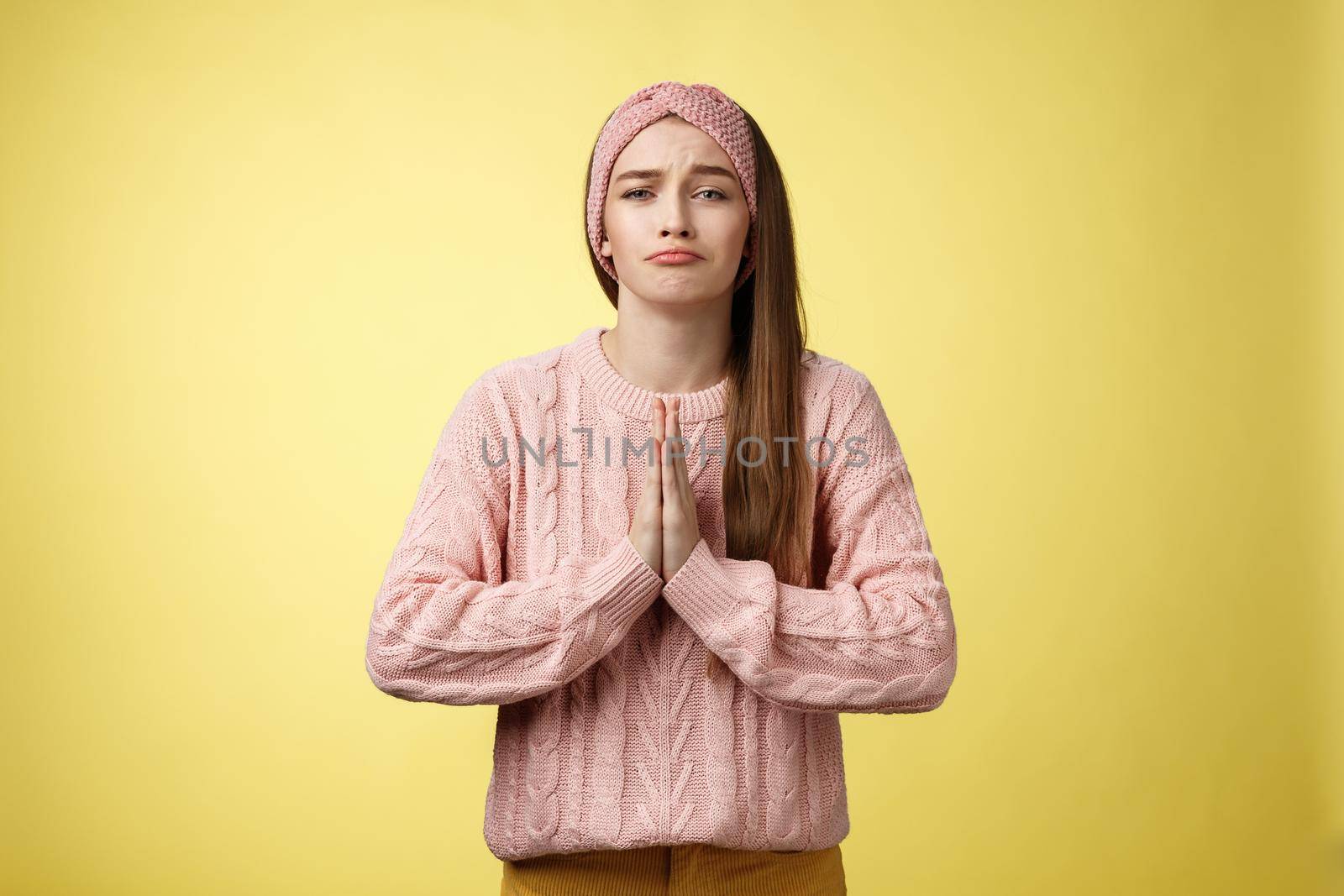 Deliberately sad girl in sweater pressing palms together in pray pouting praying for help, asking favor, begging friend lend cute dress for date, smiling silly, want something over yellow background by Benzoix