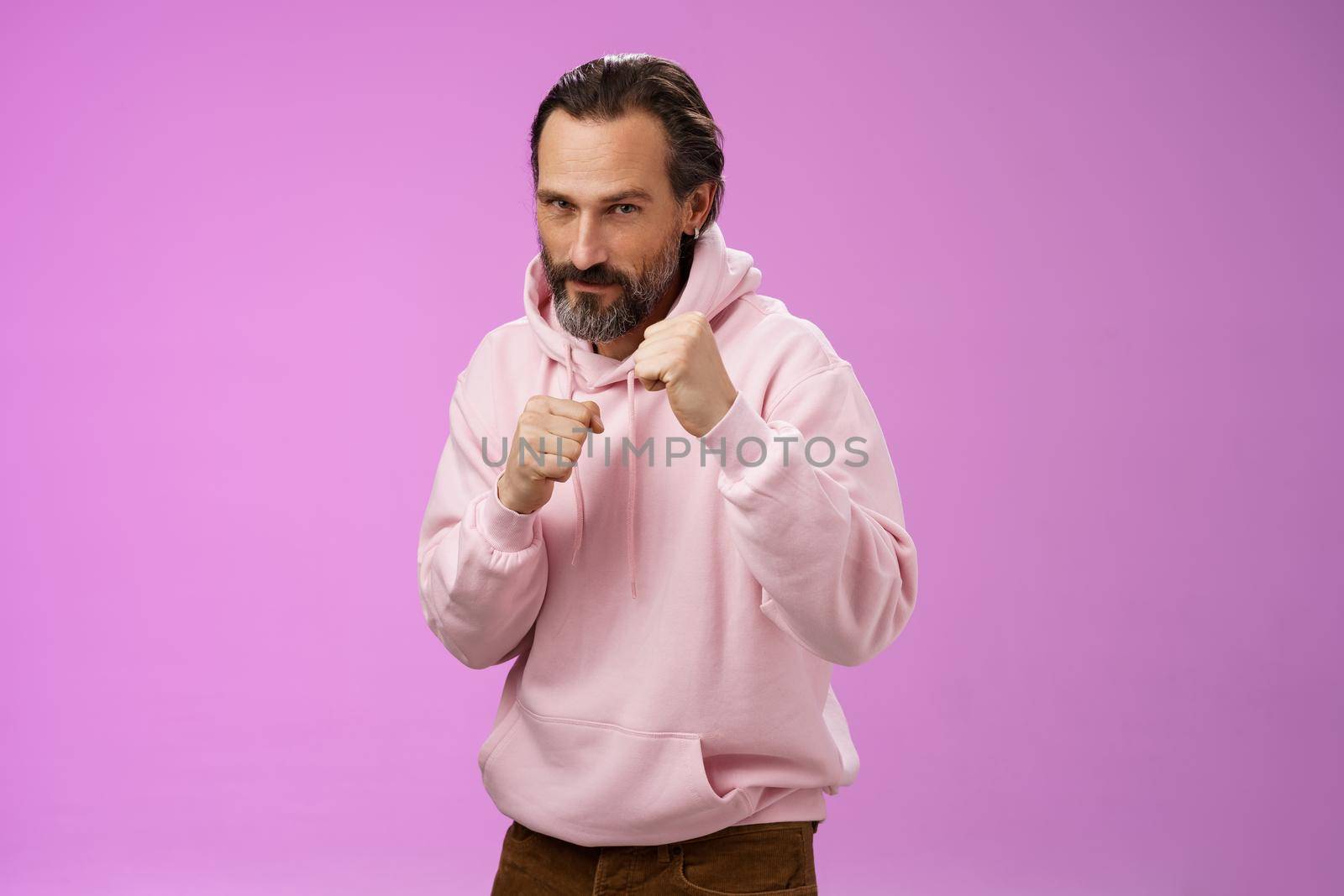 Sassy confident good-looking mature caucasian bearded man in pink hoodie teaching son how stand back fight defend himself raise fists ready boxing smiling daring, stay good shape, purple background.
