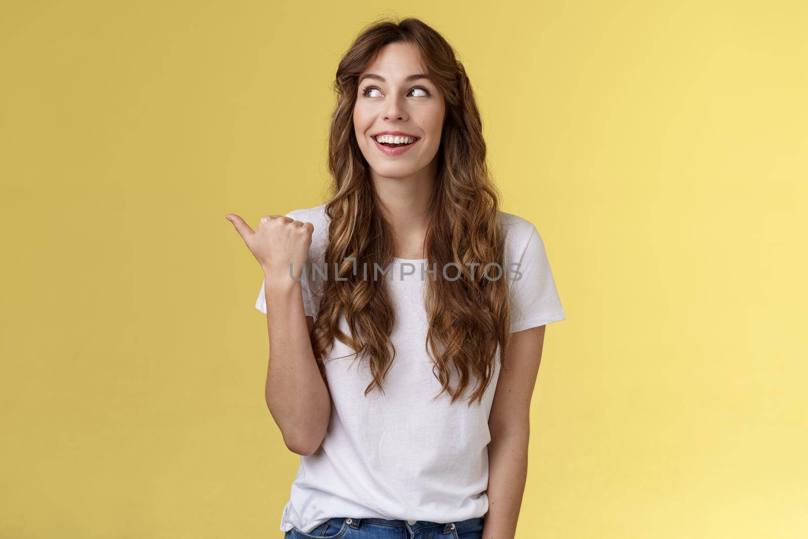 Something interesting right there. Curious lively enthusiastic charming woman glancing pointing thumb left smiling broadly discuss cool event laughing carefree stand yellow background by Benzoix