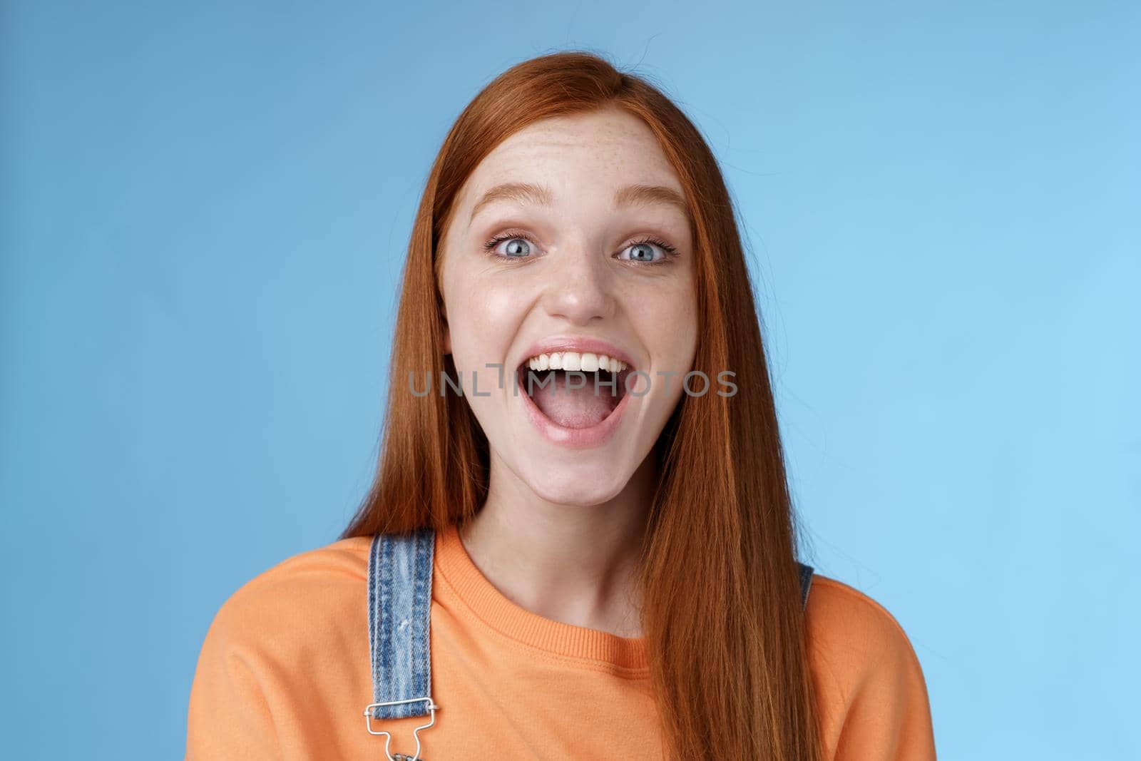 Amused charismatic lively outgoing ginger girl thrilled having fun friends yelling say a showing perfect white smile enjoy friendly joyful atmosphere standing excited positive blue background by Benzoix