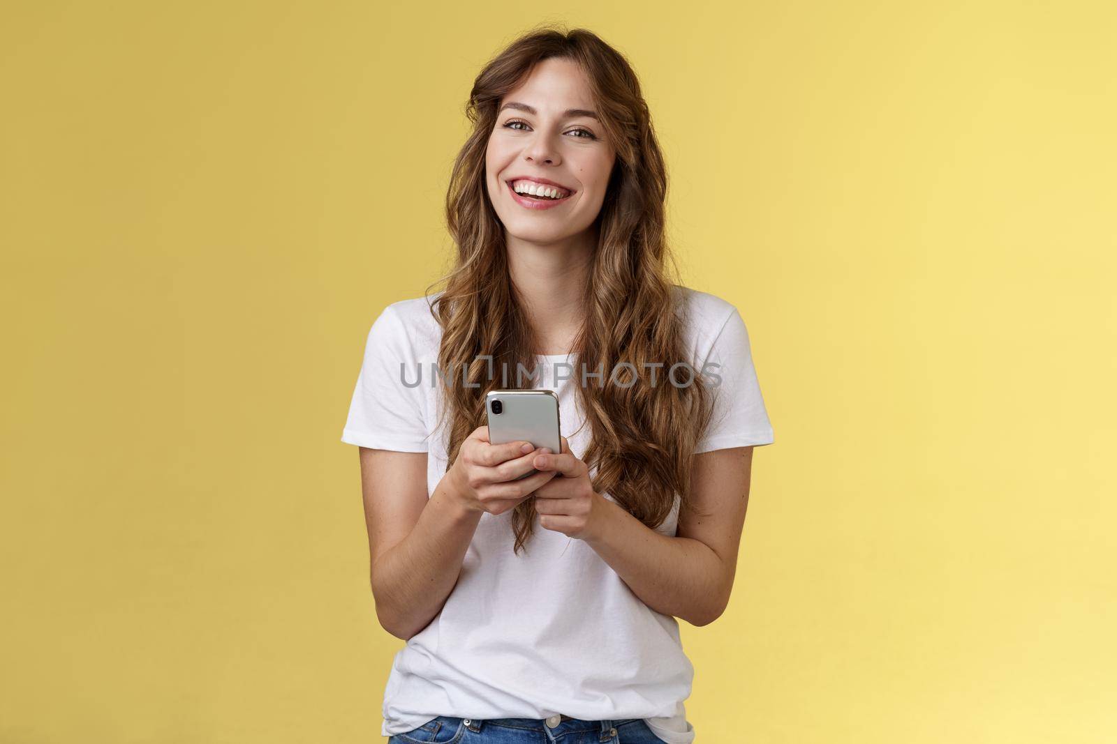 Lively enthusiastic friendly smiling happy woman using smartphone texting messaging friend checking social media feed browsing internet hold mobile phone laughing happily yellow background by Benzoix
