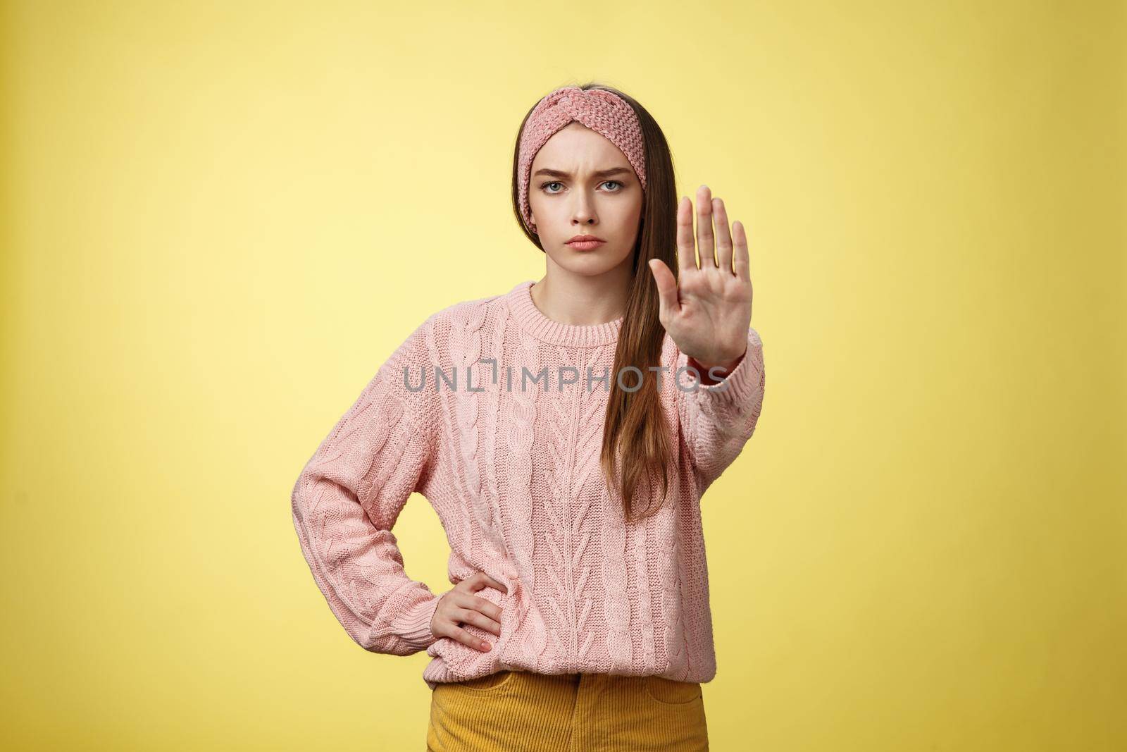 Stop it. Serious-looking confident focused young cute girl extending arm hold, tresspass gesture, frowning displeased, standing bossy denying, forbidding pass, unwilling let-through over yellow wall.
