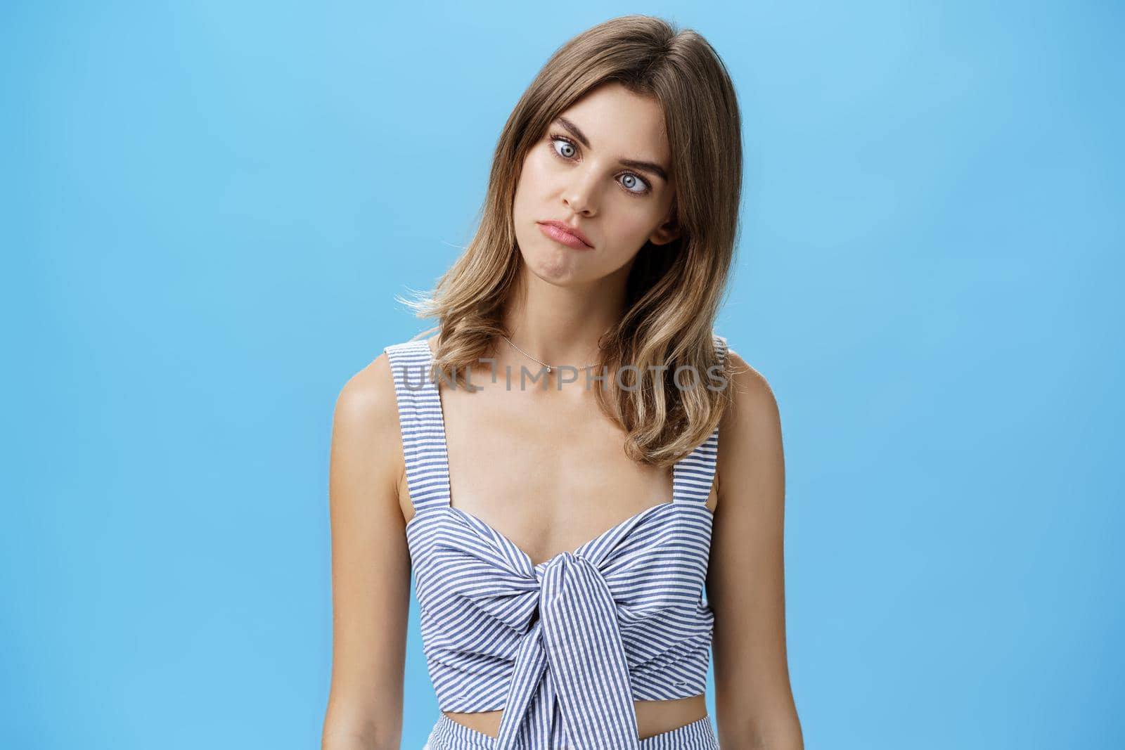 Funny girl squinting eyes to look at nose standing cute and silly over blue background in matching outfit fooling around from boredom trying spent free time aping, posing over blue background. Emotions concept