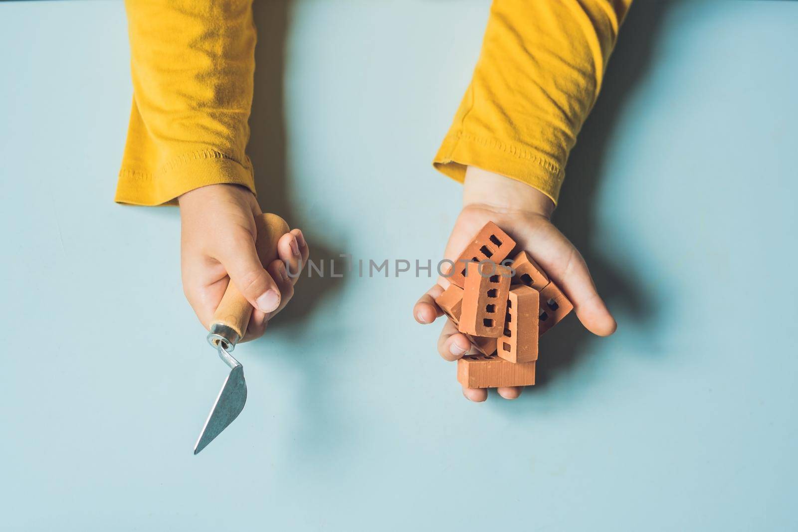 Close up of child's hands playing with real small clay bricks at the table. Toddler having fun and building out of real small clay bricks. Early learning. Developing toys. Construction concept.