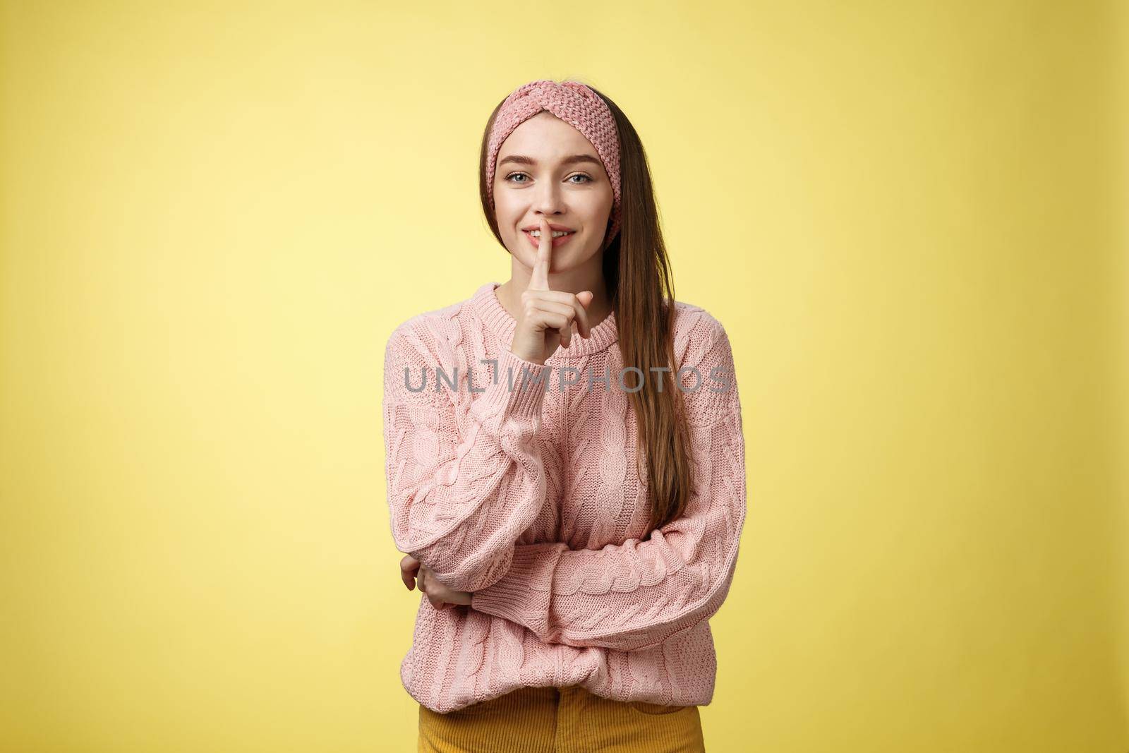 Shh keep voice down. Attractive glamour young stylish schoolgirl having secrets showing shush gesture, holding index finger on mouth smiling, hiding surprise asking not tell anyone over yellow wall by Benzoix