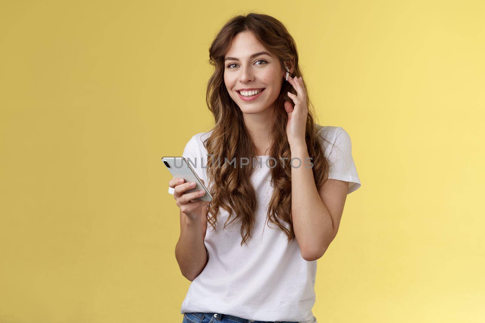 Stylish good-looking carefree urban girl put on earphones listen music wireless earbud touch headphone smiling delighted camera found awesome new track hold smartphone listen music. Lifestyle.