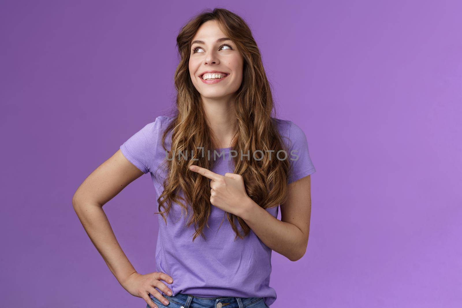 Cheerful motivated enthusiastic upbeat curly-haired girl turn left pointing sideways contemplate produly good choice smiling delighted having perfect summer day stand purple background by Benzoix