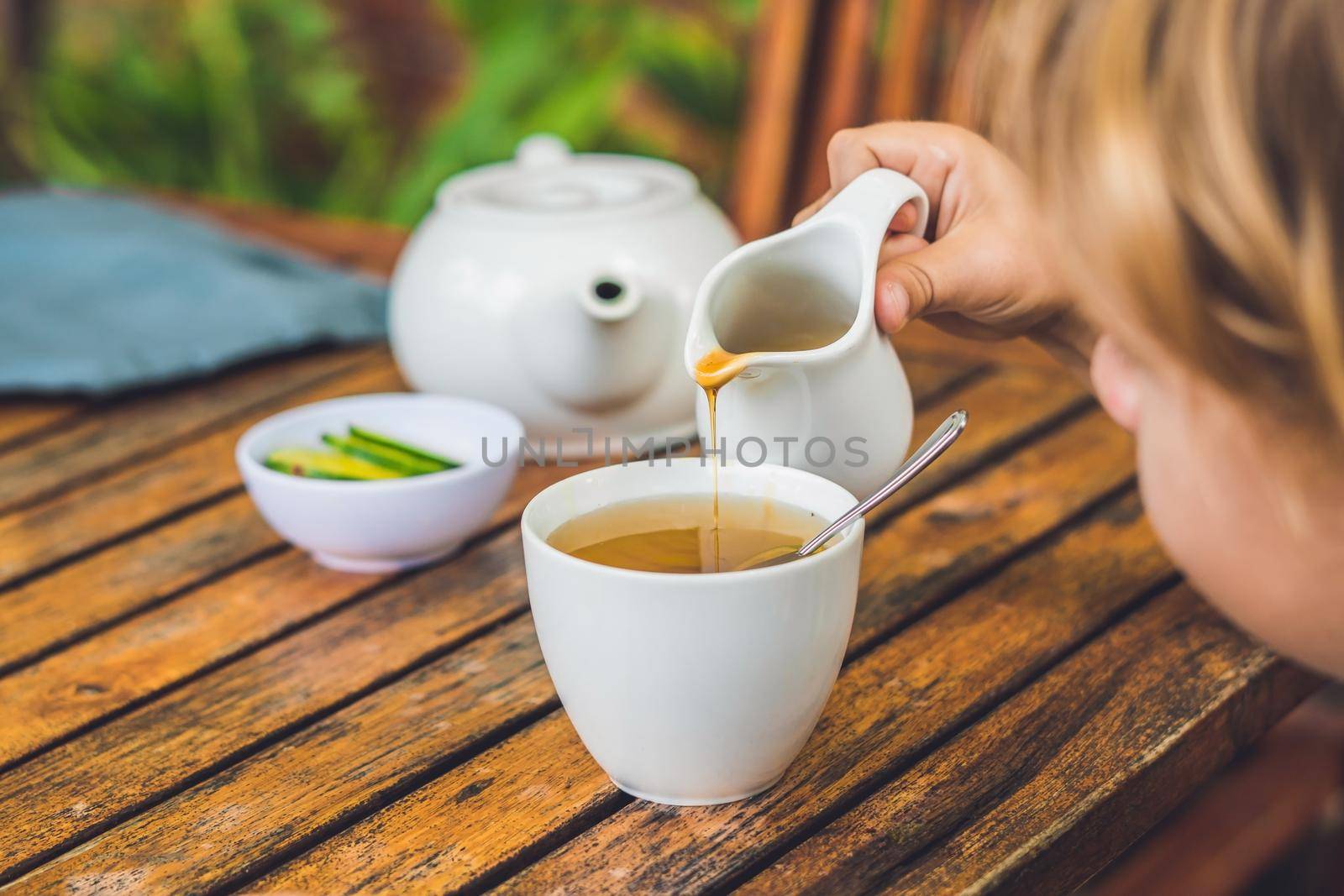 Happy nice boy pours honey into the tea in summer green garden. Portrait. outdoor.