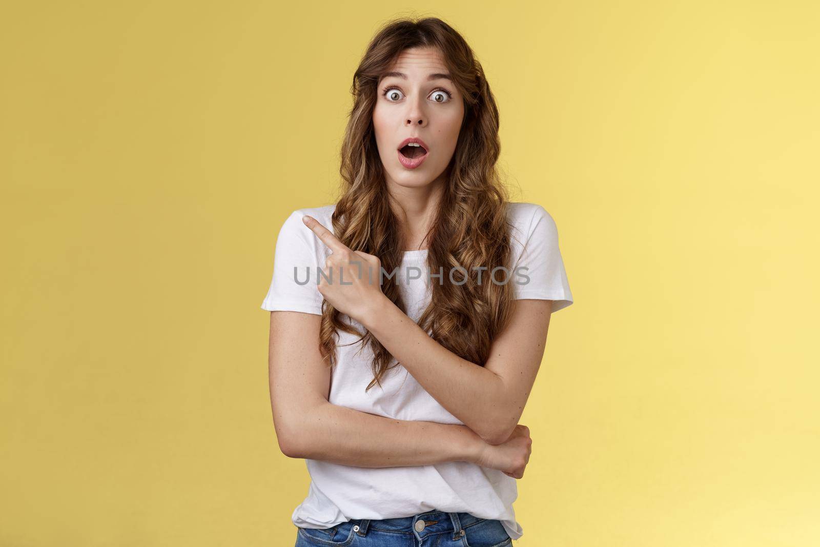 Excited impresseed speechleess shocked girl loose speech drop jaw gasping astonished asking friend advice how react stare camera opened mouth pointing left stand yellow background ambushed by Benzoix