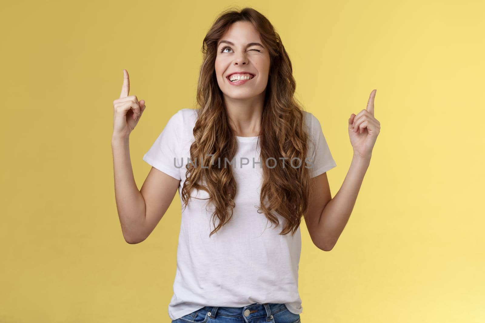 Cheeky confident positive attractive female optimistic joyful vibe smiling toothy wink grinning look up sassy pointing top making deal god hinting making cunning mood stand yellow background. Lifestyle.