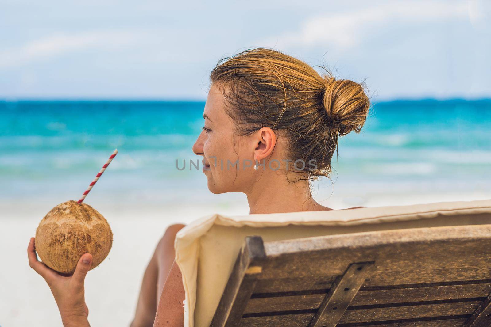 Young woman drinking coconut milk on Chaise-longue on beach. by galitskaya