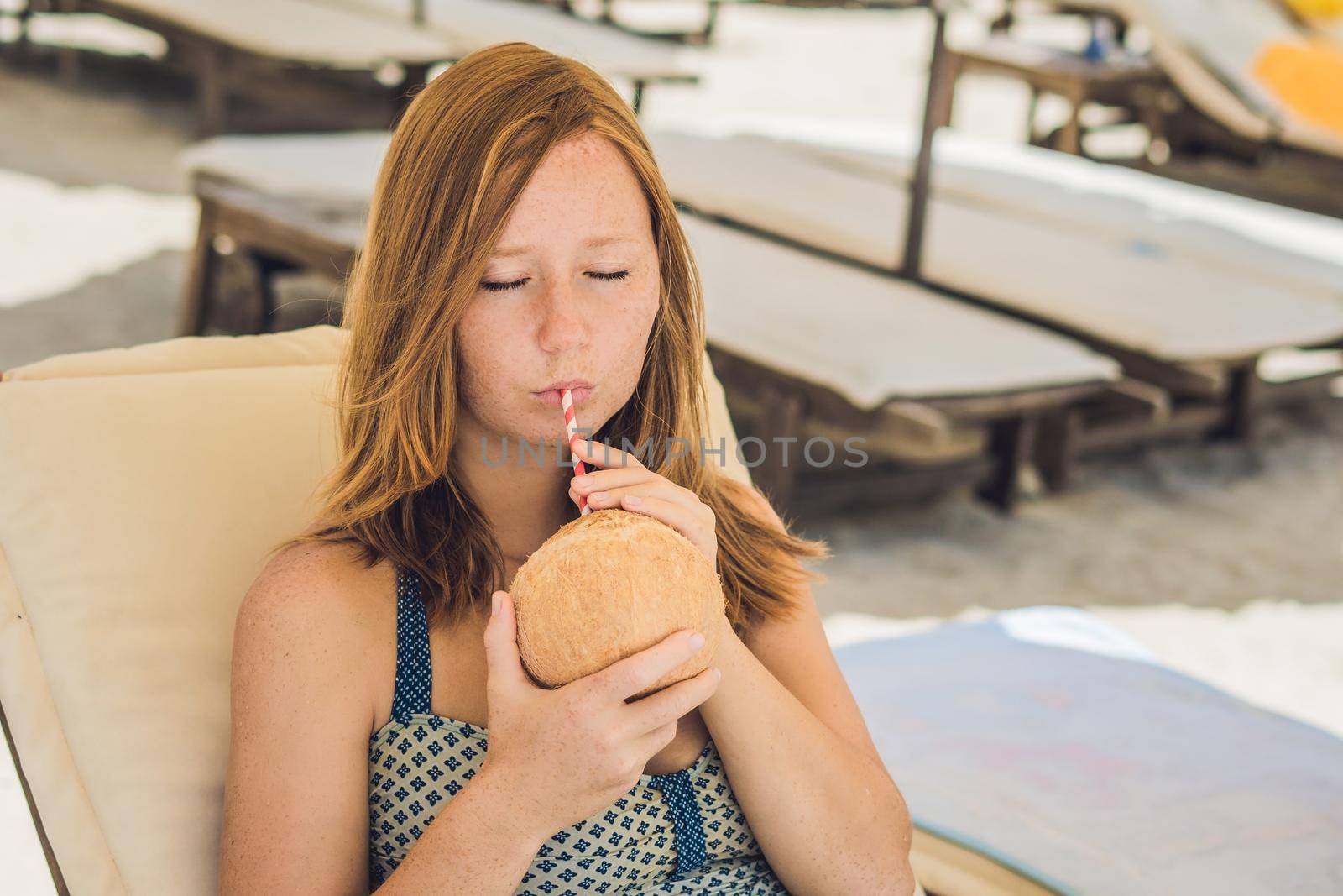 Young woman drinking coconut milk on Chaise-longue on beach. by galitskaya