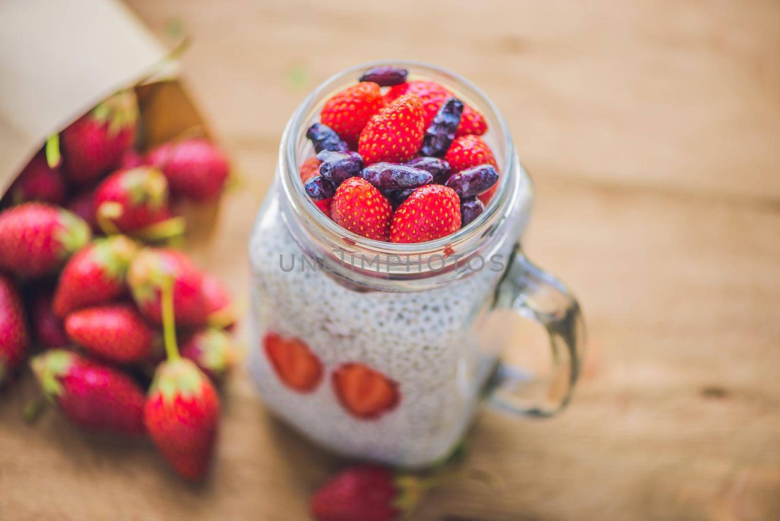 Healthy layered dessert with chia pudding, strawberry and honeysuckle in a mason jar on rustic background.