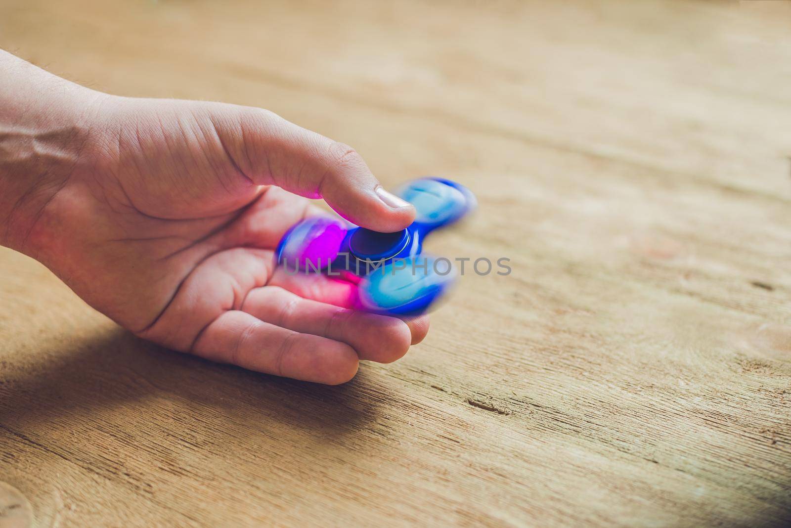 A man hand holding hand spinner or fidget spinner over wooden background by galitskaya