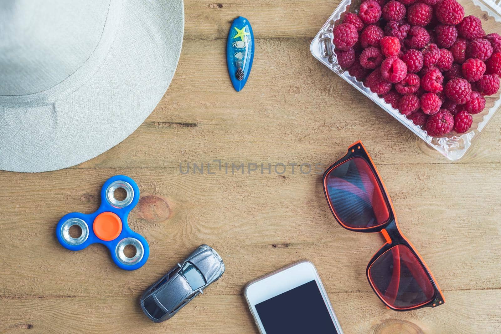 Summer holiday, vacation, relaxation concept. Raspberries, hat, mobile phone, smartphone, spinner, sunglasses from above, top view, flat lay on wooden background. Colorful background with free text copy space. Summer vibes concept.