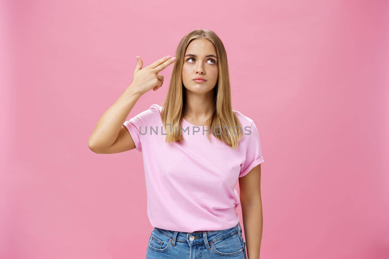 Someone kill me please. Annoyed and bored fed up cute emotive young woman with tanned skin chubby face and fair hair rolling eyelids holding finger near head as if commiting suicide, making shot. Body language concept