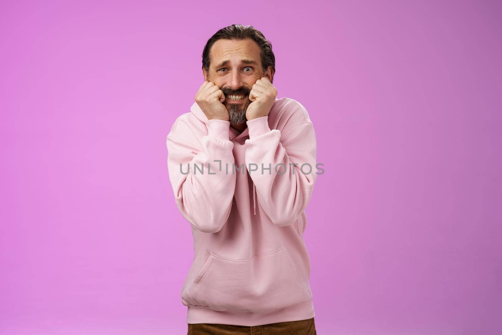 Scared insecure silly adult bearded man grey hair in pink hoodie press palms mouth bite fingers clench teeth shocked frightened widen eyes terrified standing stupor horrified, purple background by Benzoix