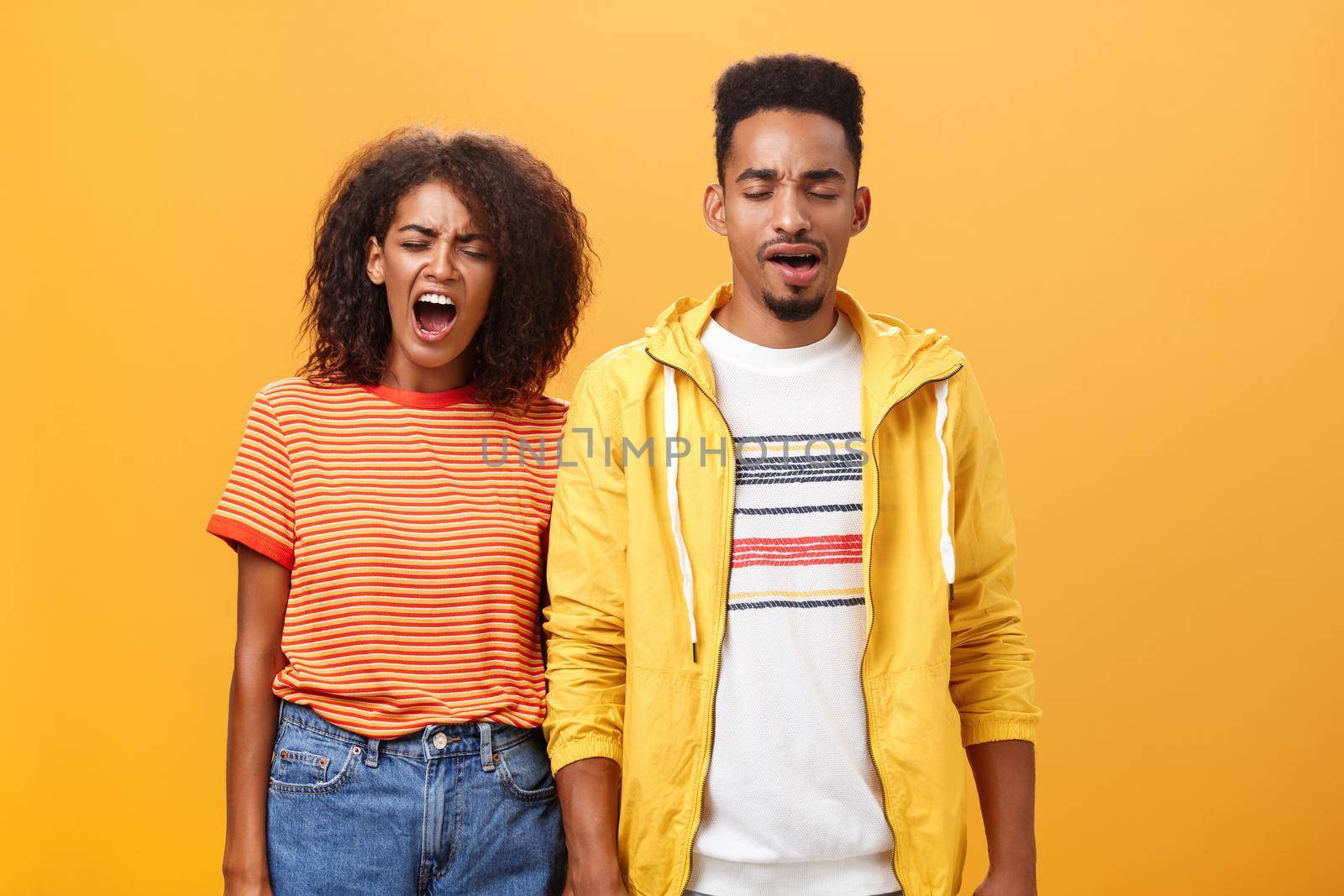Stylish and attractive brother and sister over orange background yawning with closed eyes and tired expression being drained and exhausted after dealing with house chores cleaning mess after party. Lifestyle.