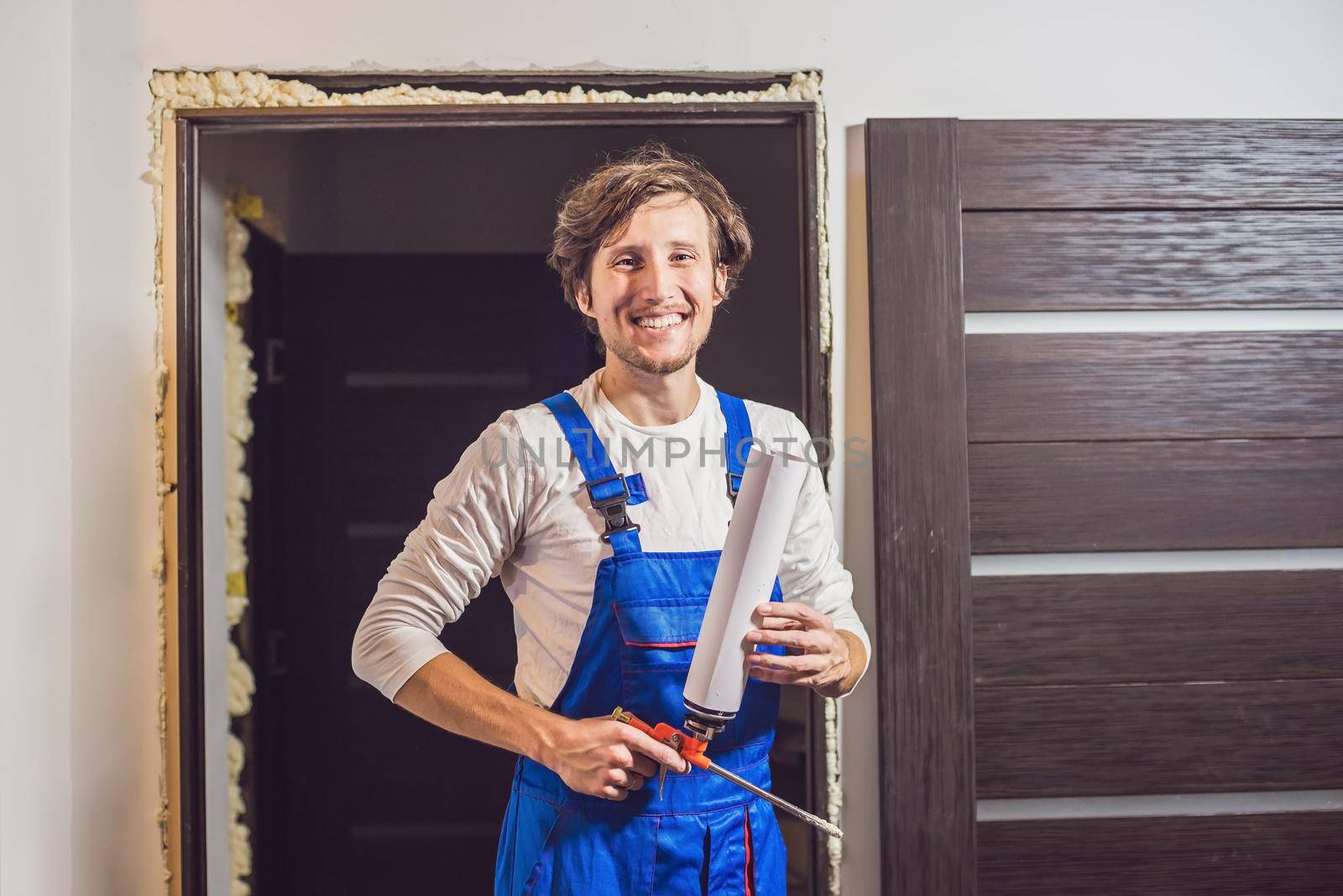 Young handyman installing door with an mounting foam in a room by galitskaya