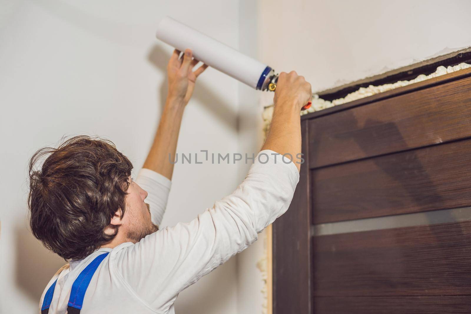 Young handyman installing door with an mounting foam in a room by galitskaya