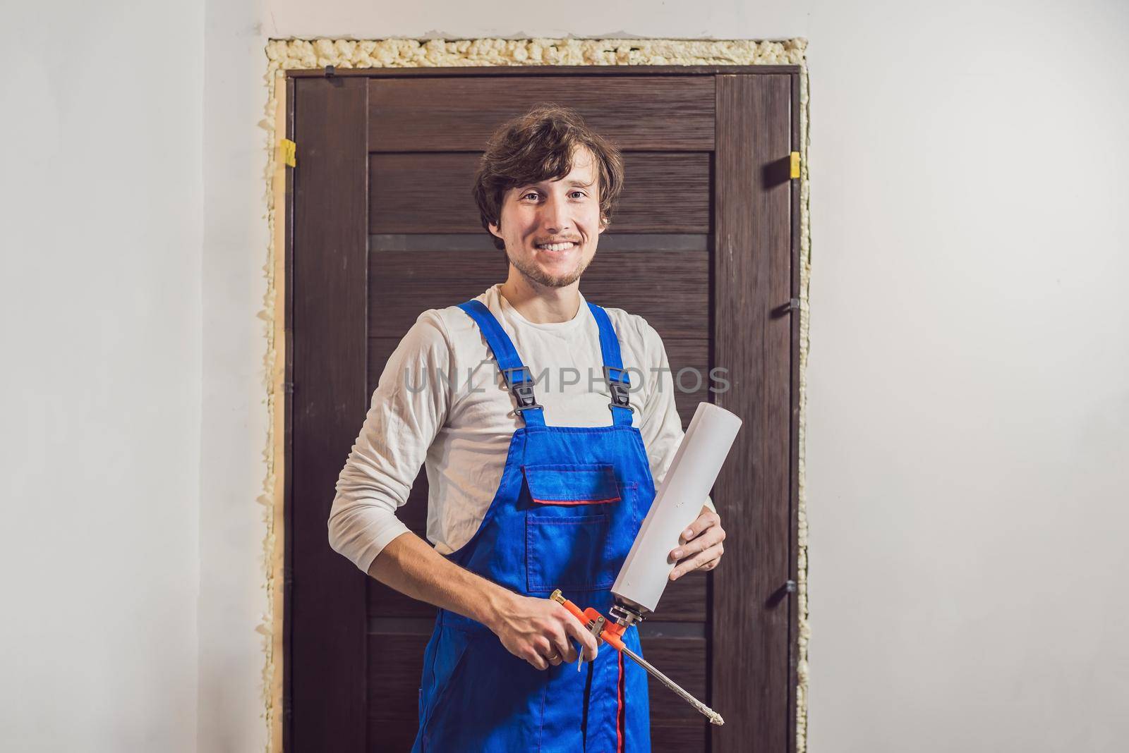 Young handyman installing door with an mounting foam in a room by galitskaya