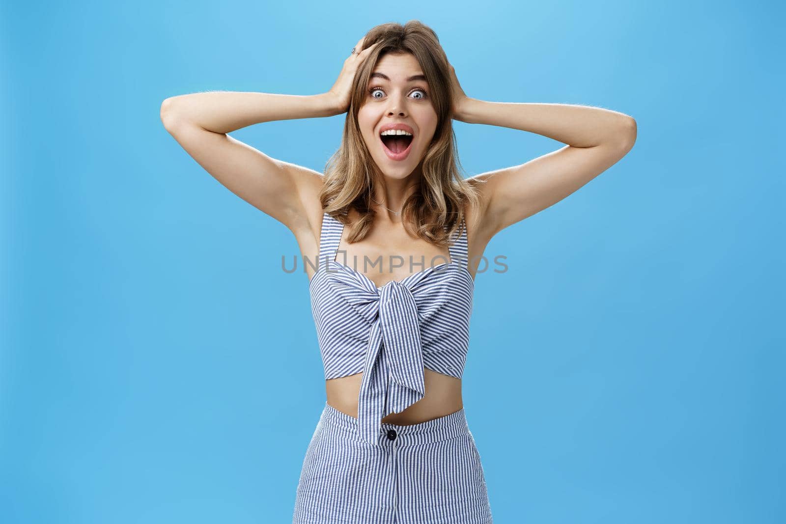Portrait of cheerful and surprised emotive charismatic attractive young woman with medium natural hairstyle holding hands on hair and smiling broadly feeling astonished with unexpected surprise. Lifestyle.