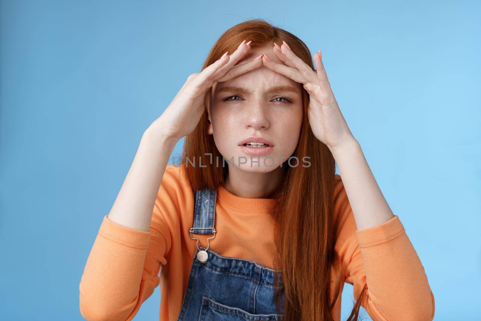 Puzzled unsure cute funny redhead european woman searching someone squinting cannot see without glasses peer into distance hold hands forehead cover sight sunlight, standing blue background.