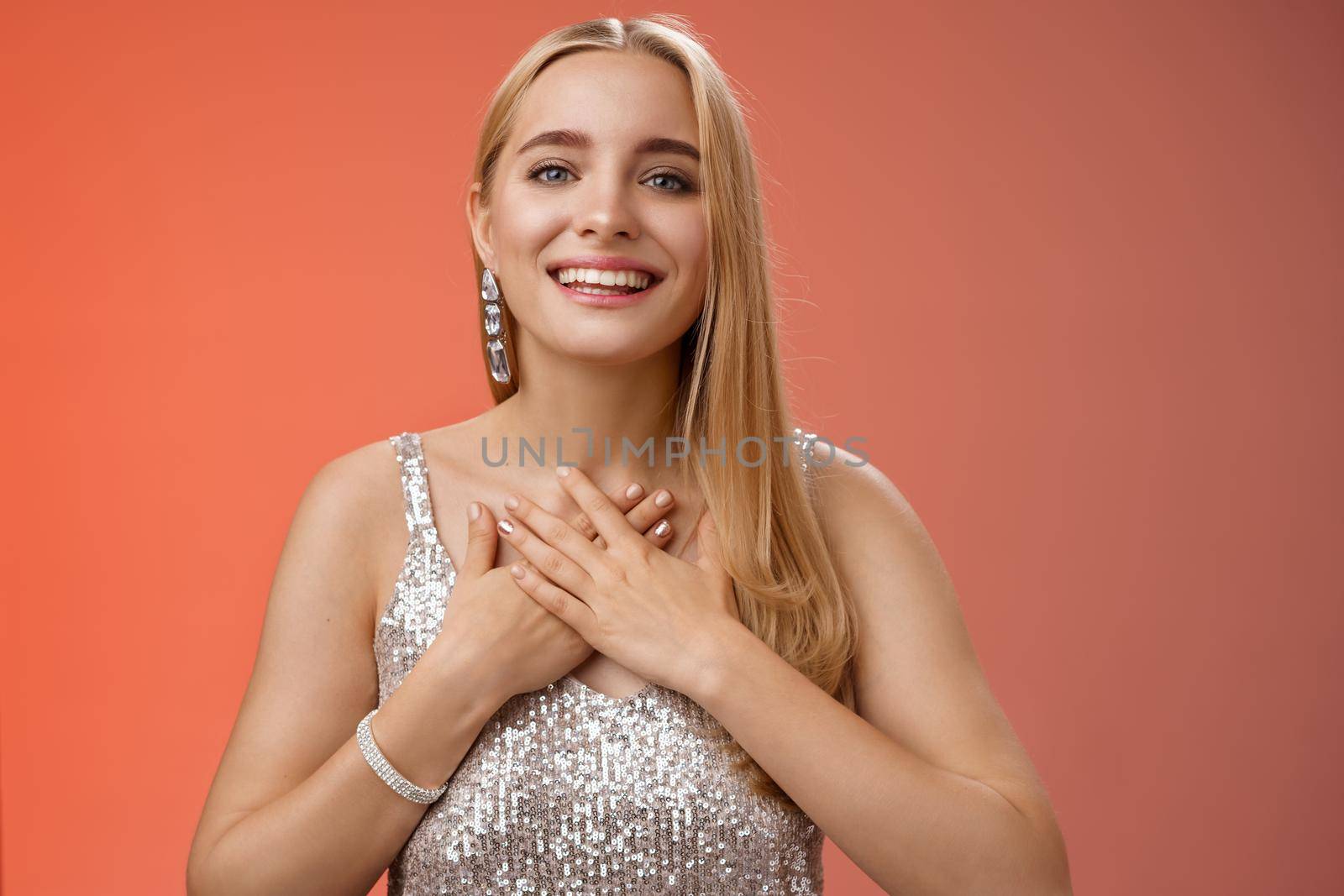 Grateful charming blond european 25s woman in silver party dress press palms heart feel thankful appreciate effort cherish romantic gesture receive flattering compliments gifts, smiling happily by Benzoix