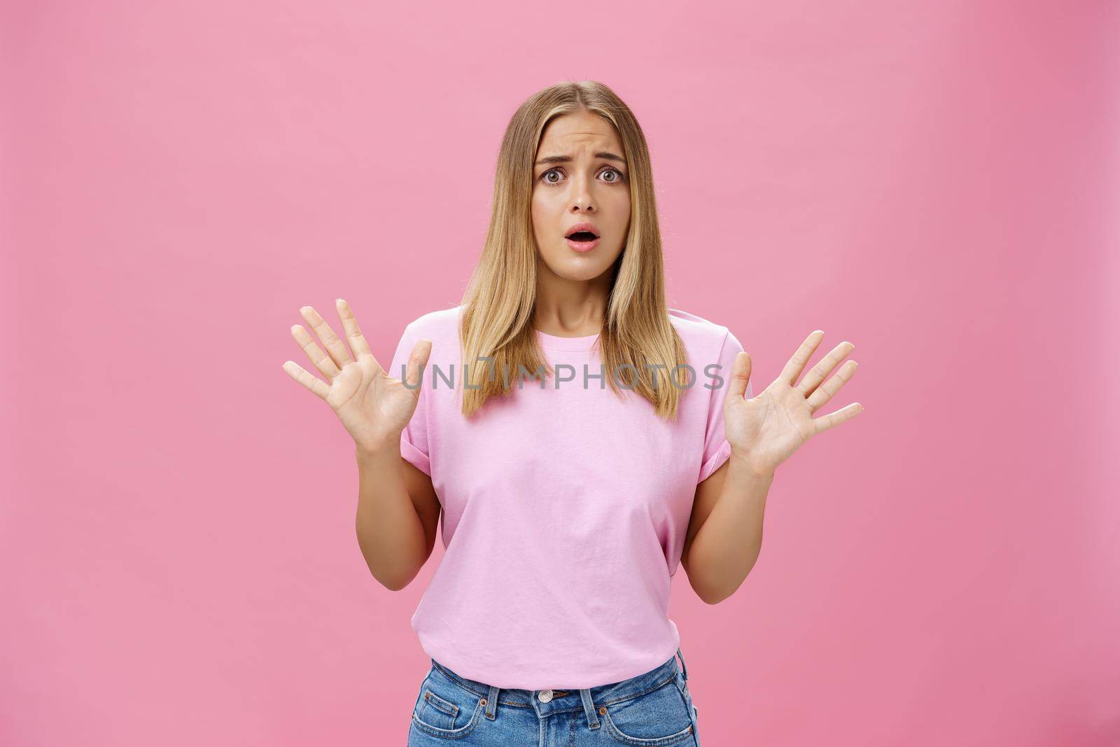 Woman looking nervous explaining with panicking gestures she not involved frowning opening mouth and gasping feeling concerned and worried waving hands over chest posing against pink wall. Copy space