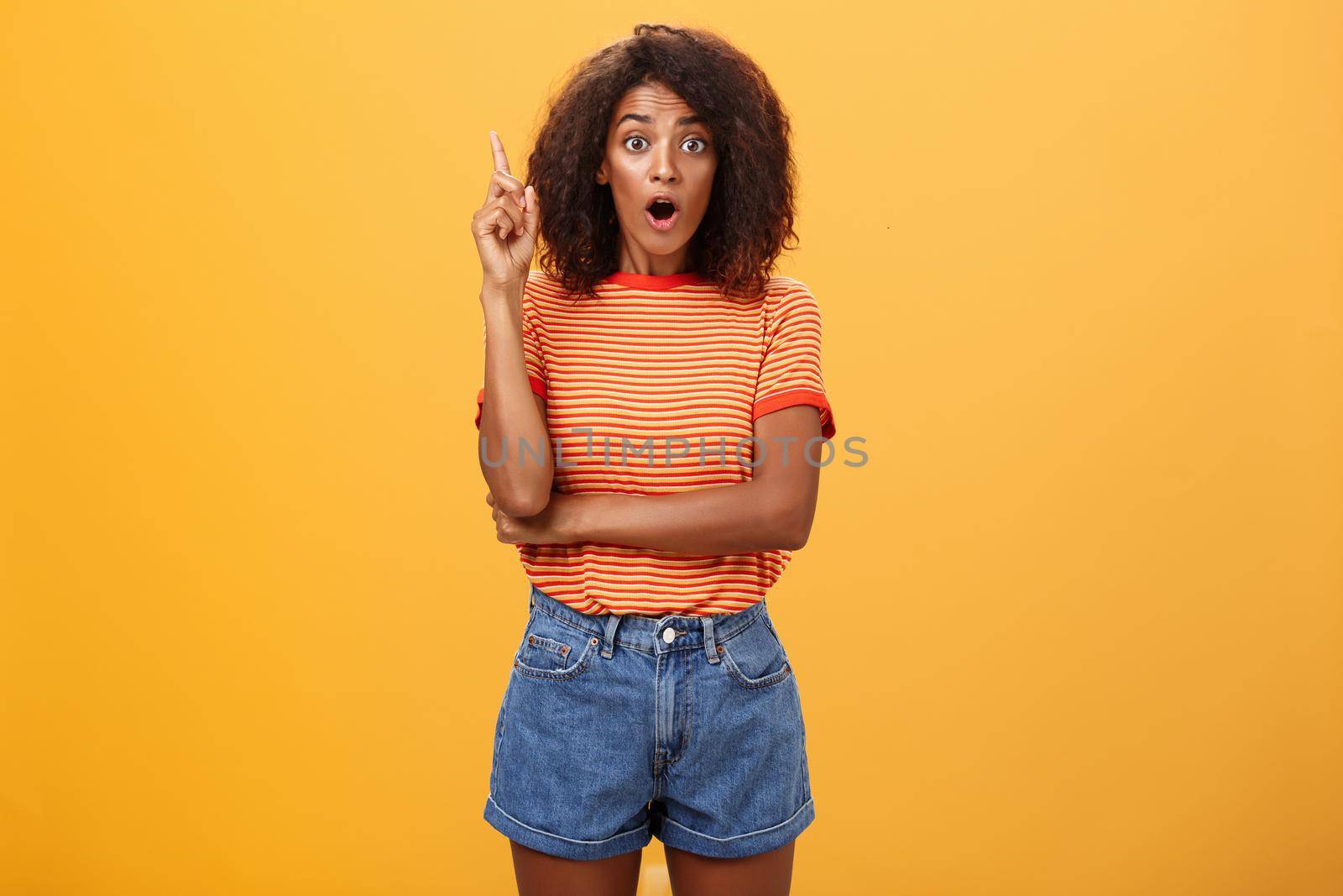 Girl finally understood riddle adding suggestion outloud. Excited thrilled good-looking dark-skinned woman staring amazed raising index finger in eureka gesture having idea over orange wall. Emotions and body language concept