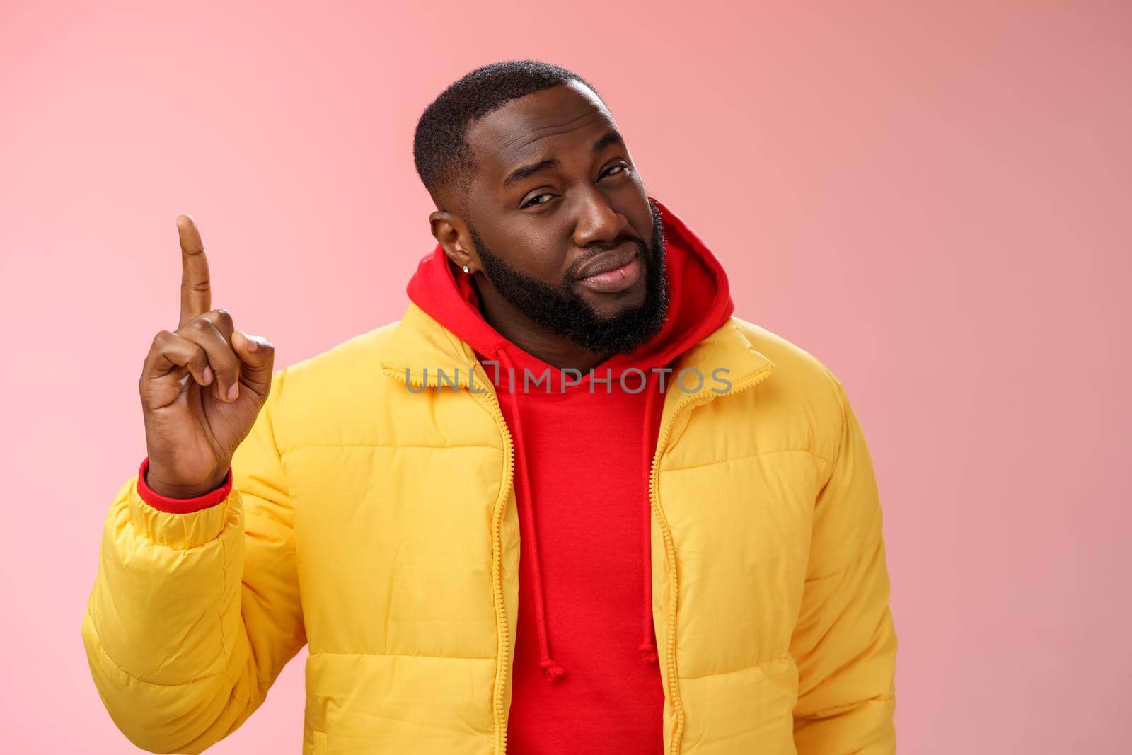 Doubtful displeased african american bearded male customer pointing up index finger squinting cringing disbelief hesitant uncertain product quality, standing questioned frustrated pink background.