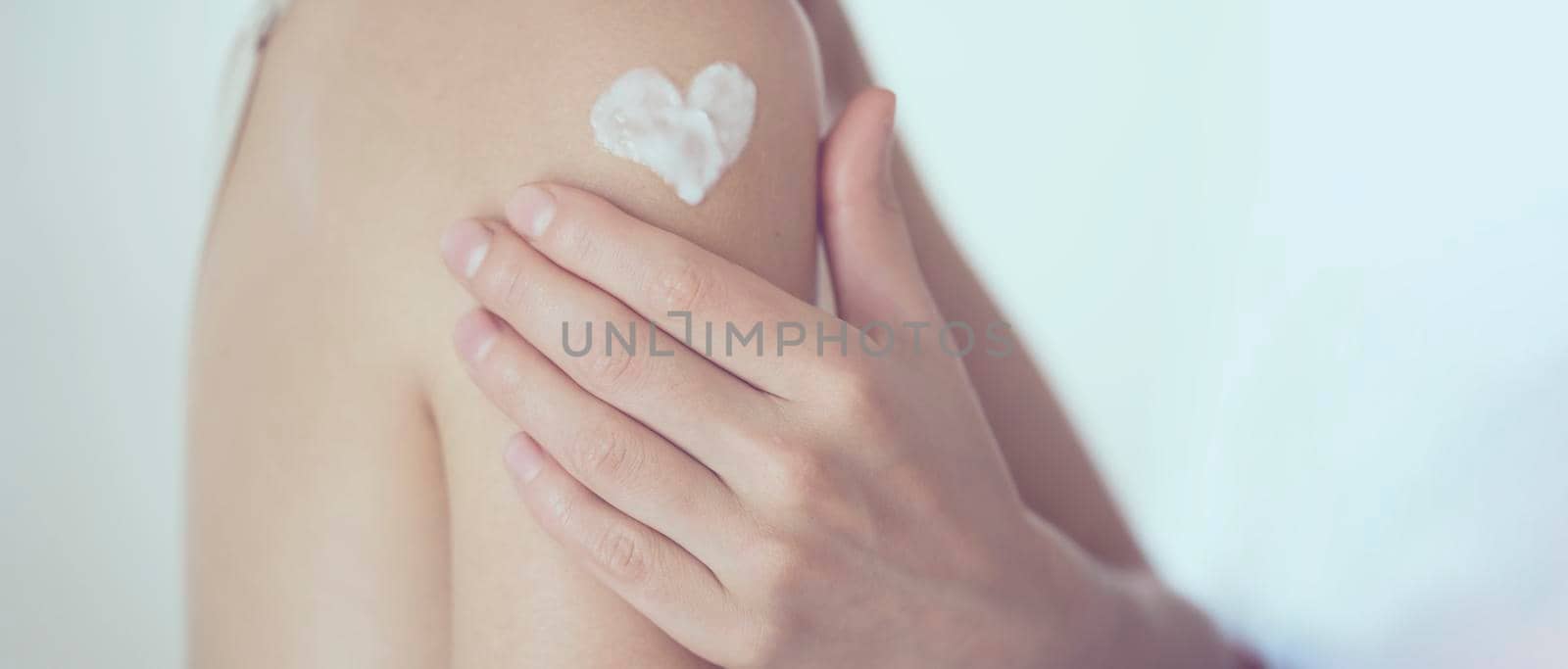 A young girl applies a moisturizer to her skin, a woman gently cares for her body, depicts a heart with a cream, taking care of herself, beauty and health.