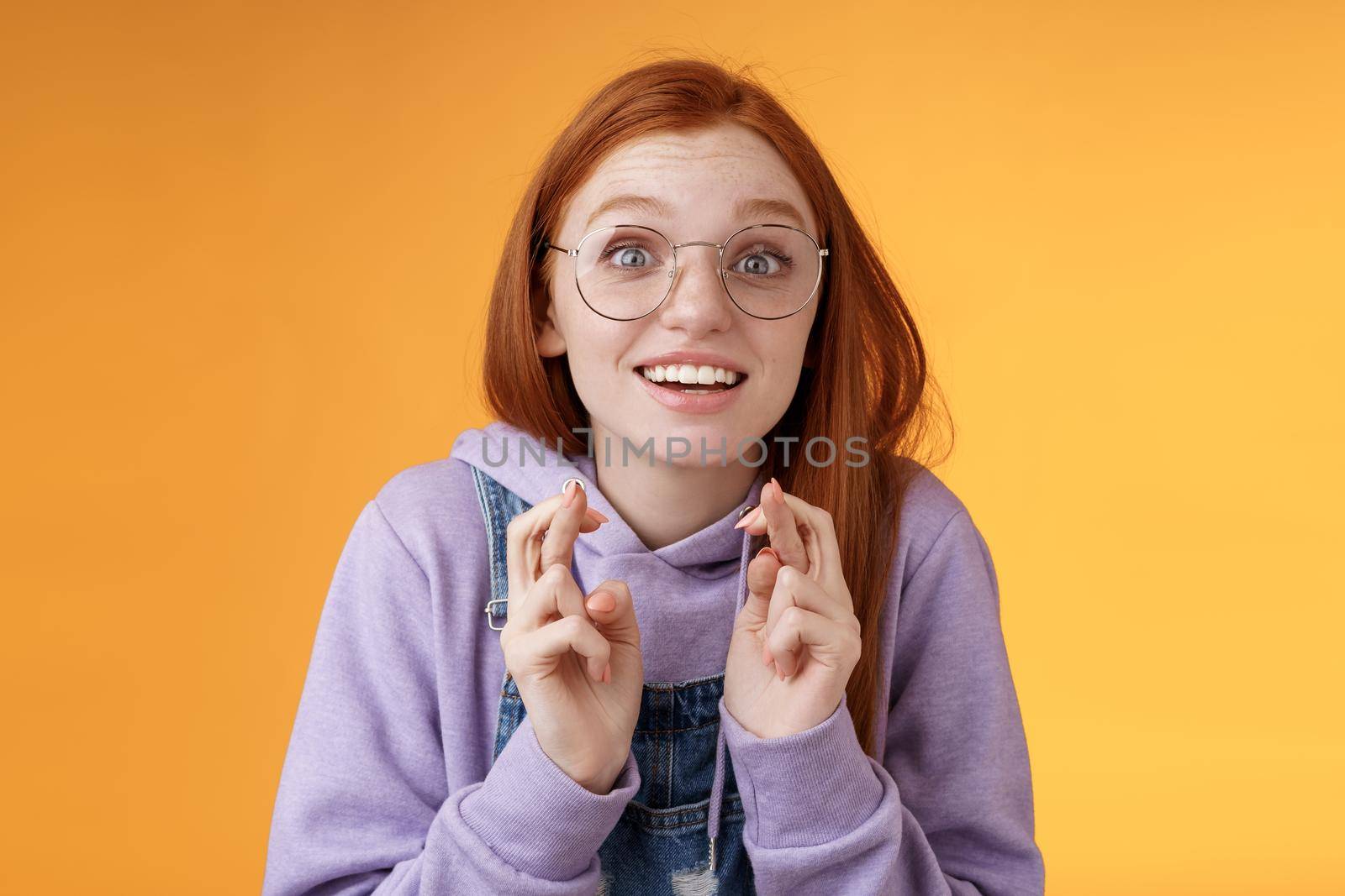 Girl excited watching results cross fingers good luck cheering favorite team wanna win dream come true thrilled open mouth wide stare camera hopeful supplicating desire fulfilled, orange background.