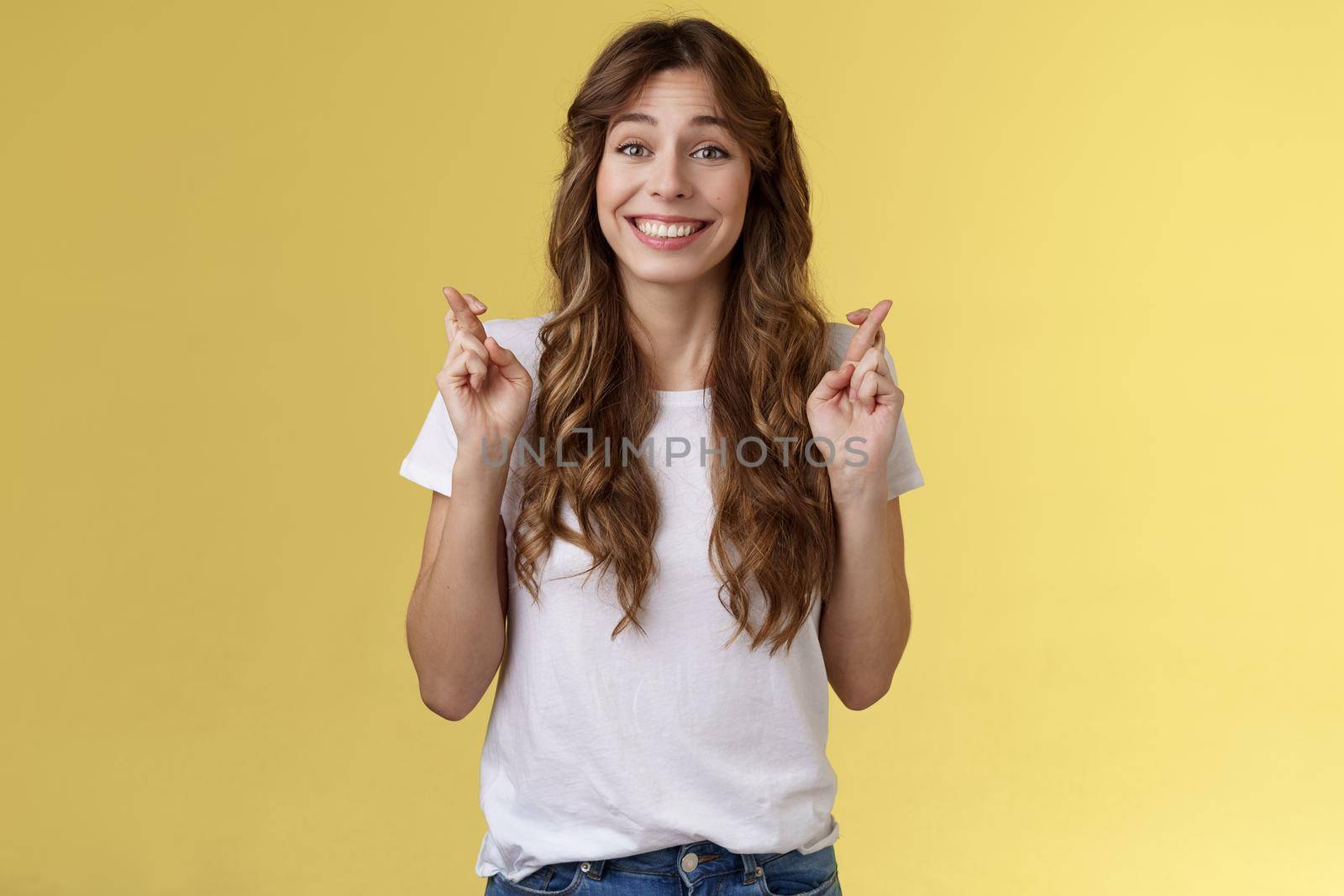 Silly hopeful excited attractive caucasian girl curly haircut wishing optimistic smiling broadly cross fingers good luck anticipating miracle grinning excited implore praying fulfill desires by Benzoix
