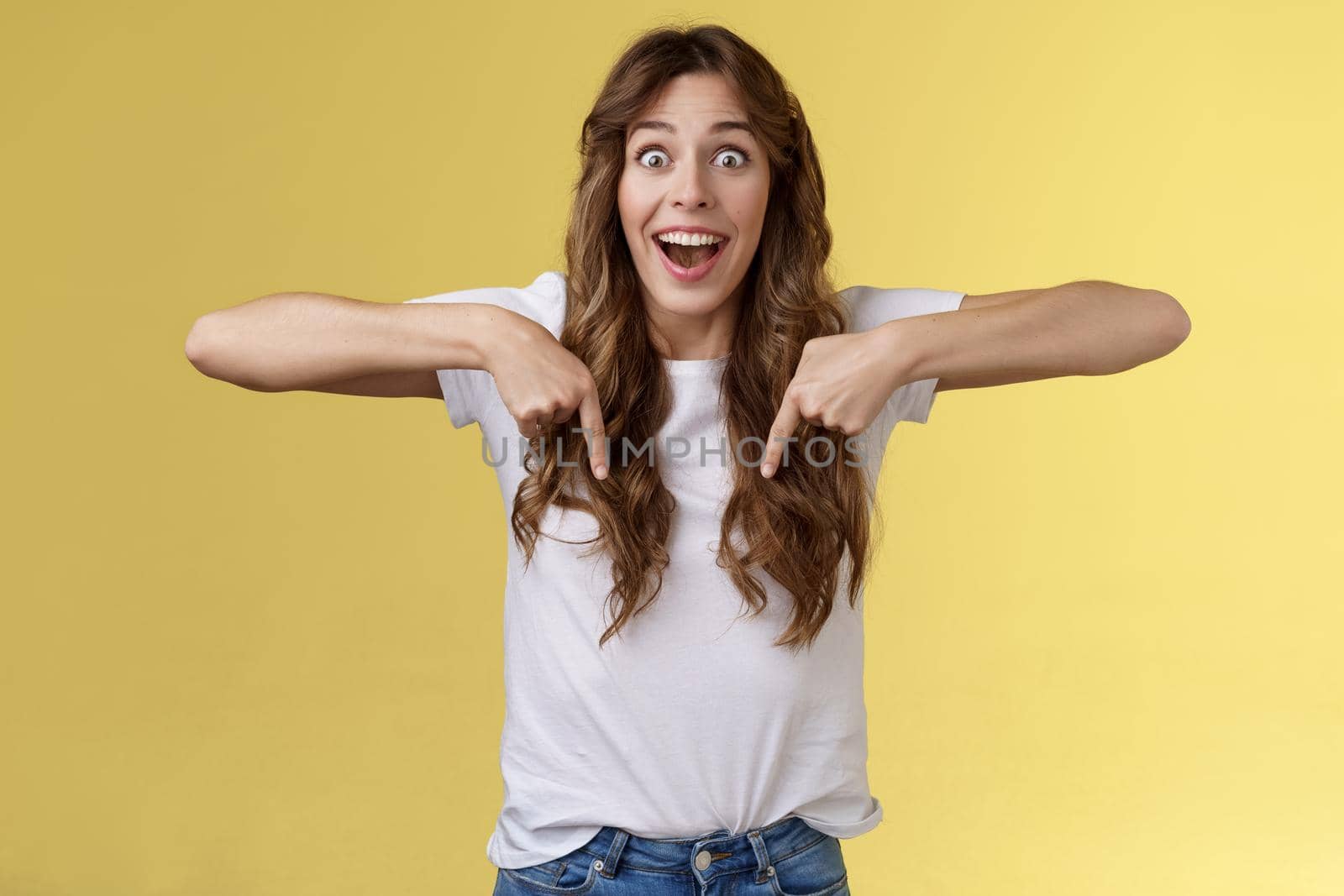 Tempting astonished impressed excited lively girl fan react stunned lose speech fascinated pointing down thrilled stare camera admiration surprise full disbelief stand yellow background.