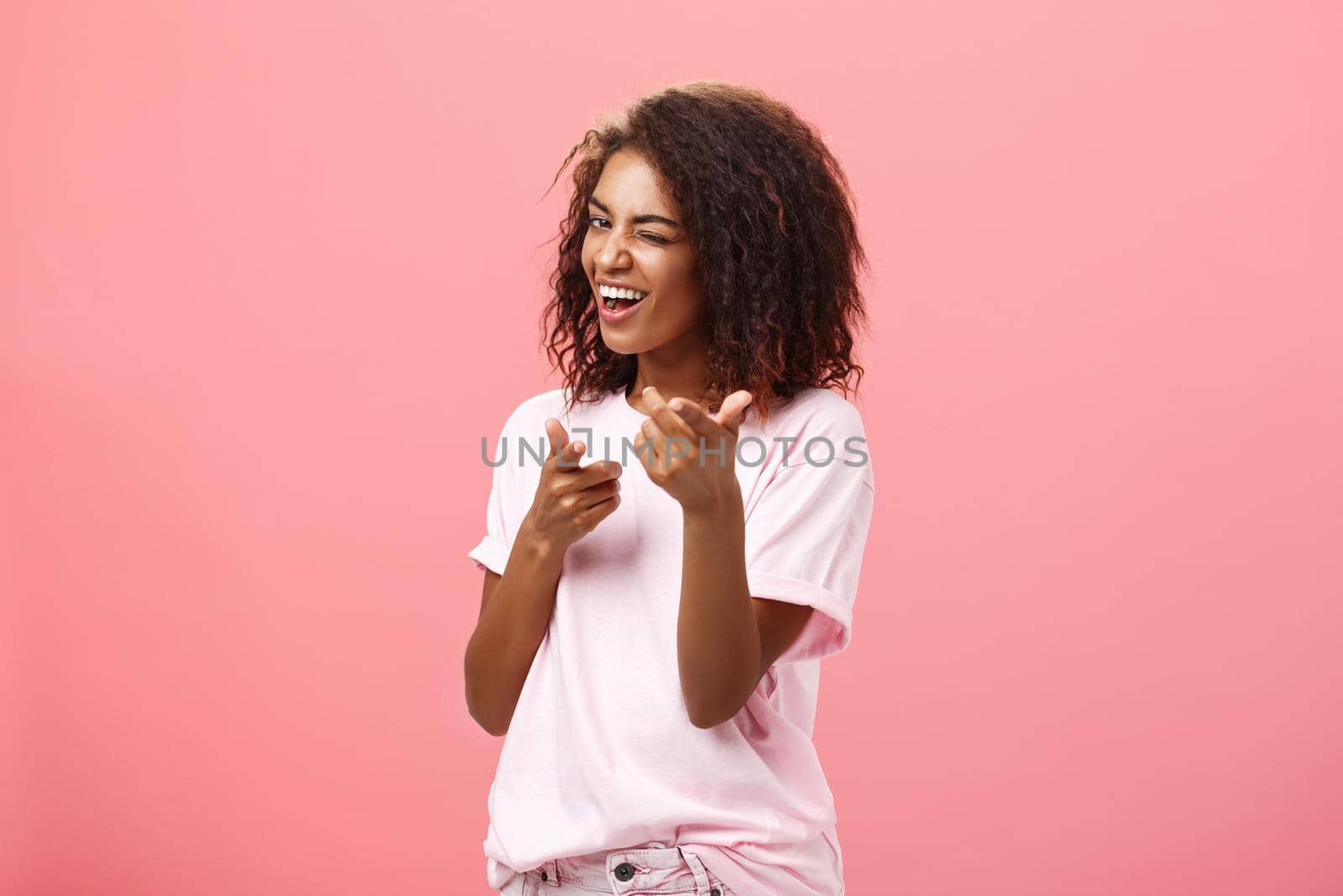 Hey you awesome. Playful charming and happy carefree dark-skinned trendy girl with curly hairstyle winking and smiling broadly making finger gun move towards camera checking out cool outfit.