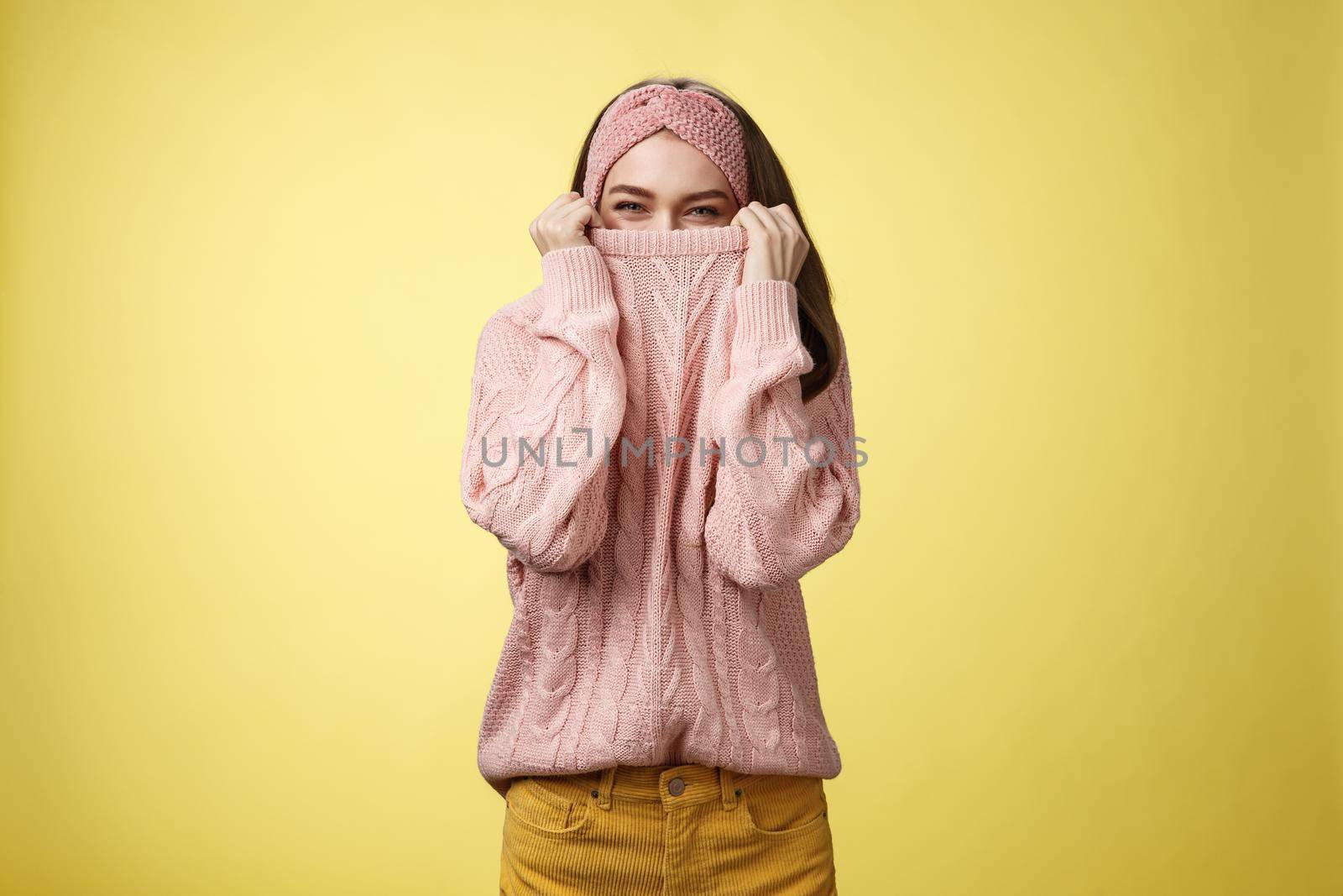 Cute playful young girl hiding in sweater peeking and squinting flirty over top of cloth pulling collar on nose, fooling around having fun happily, being in positive good mood, warming-up on cold day by Benzoix