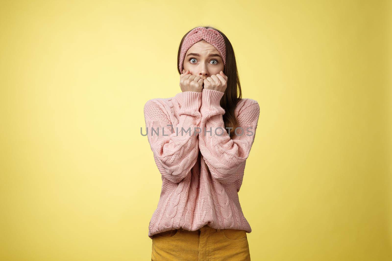 Stunned scared timid insecure cute young girl frightened gasping from fear pressing hands to mouth standing in stupor shocked, horrified stupified against yellow background being victim of abuse by Benzoix