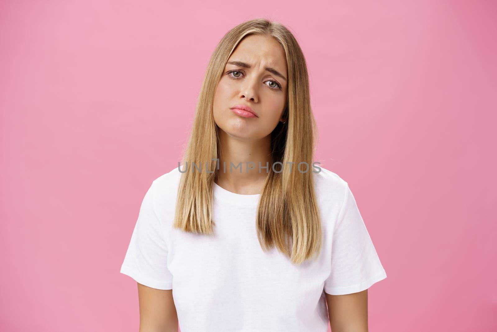 Sad girl whining tilting head raising eyebrows in upset expression and pursing lips feeling disappointed and envy, regretting missed chance standing unhappy and moody over pink background. Emotions concept