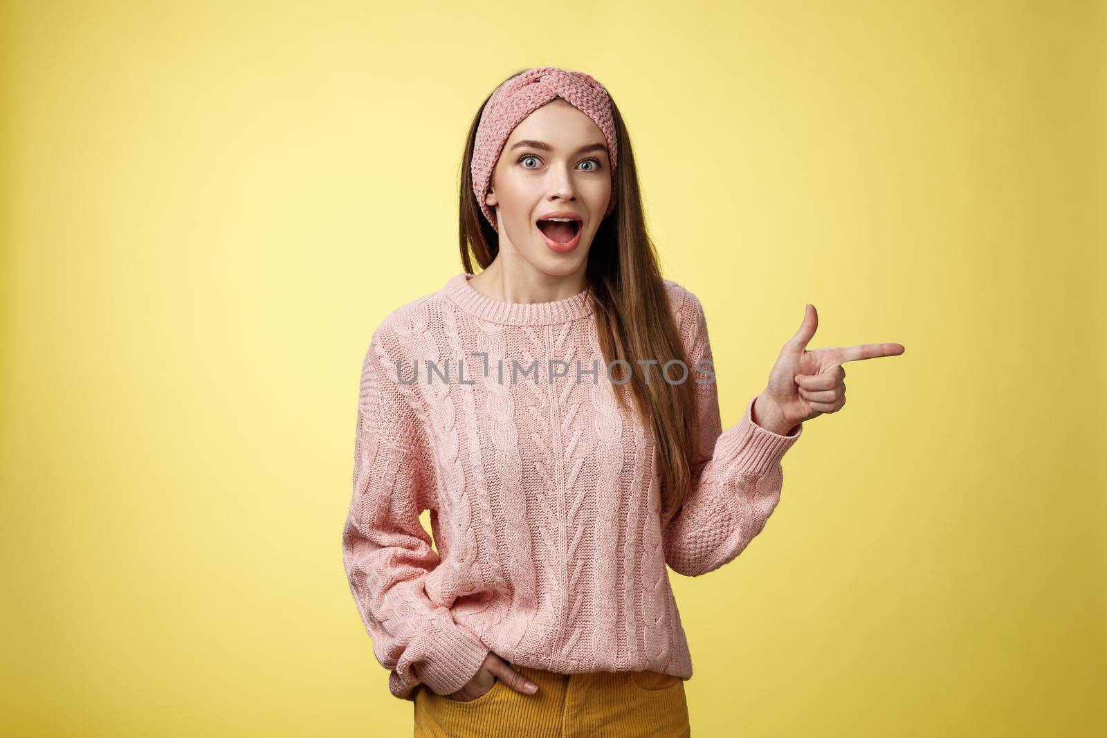 Amused thrilled attractive young female sharing amazement and excitement pointing right dropping jaw seeing unbeliavable awesome product, girl astonished advertising cool promo over yellow background.
