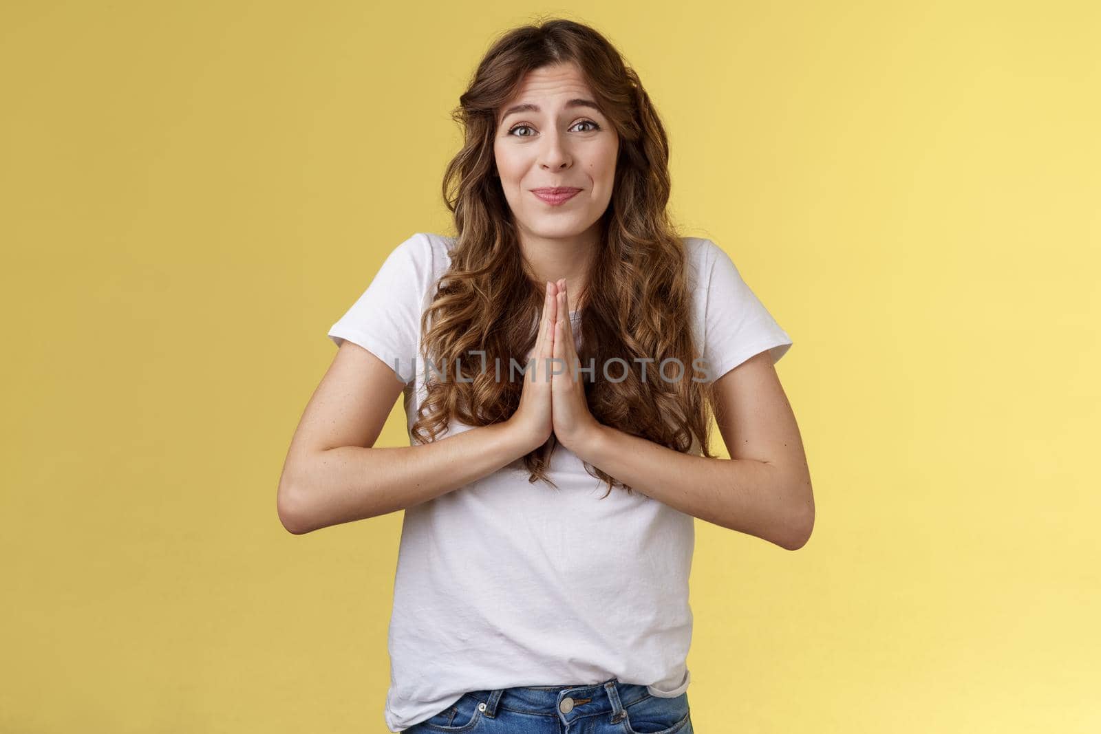 Cute hopeful young caucasian girl stooping hold hands pray smiling hope for pity begging favour plead asking advice say sorry grinning lovely making faithful glances you lend hand yellow background. Lifestyle.