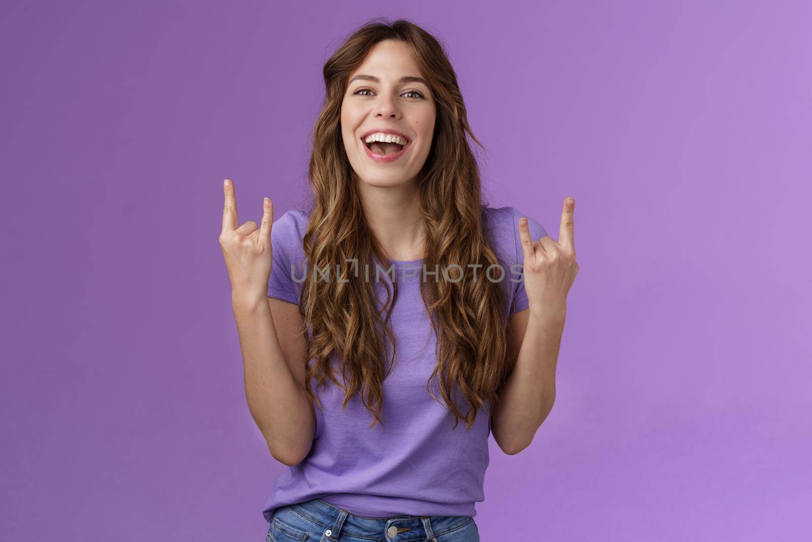 This summer holidays rock. Happy enthusiastic cheerful girl having fun enjoy awesome party weekends smiling broadly say yeah joyful make heavy-metal sign stand purple background amused by Benzoix