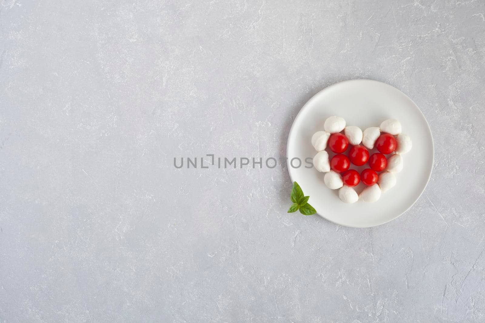 tomatoes cherry and mozzarella in a heart shape, concept of easy cooking for Valentine Day, top view, copy space