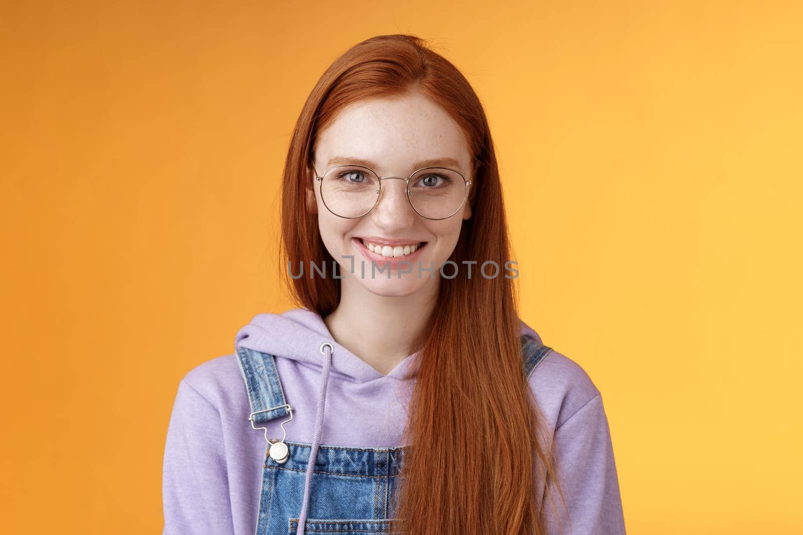 Good-looking redhead female programmer glasses hoodie smiling satisfied look professional aim success standing confident grinning delighted camera talking casually orange background.