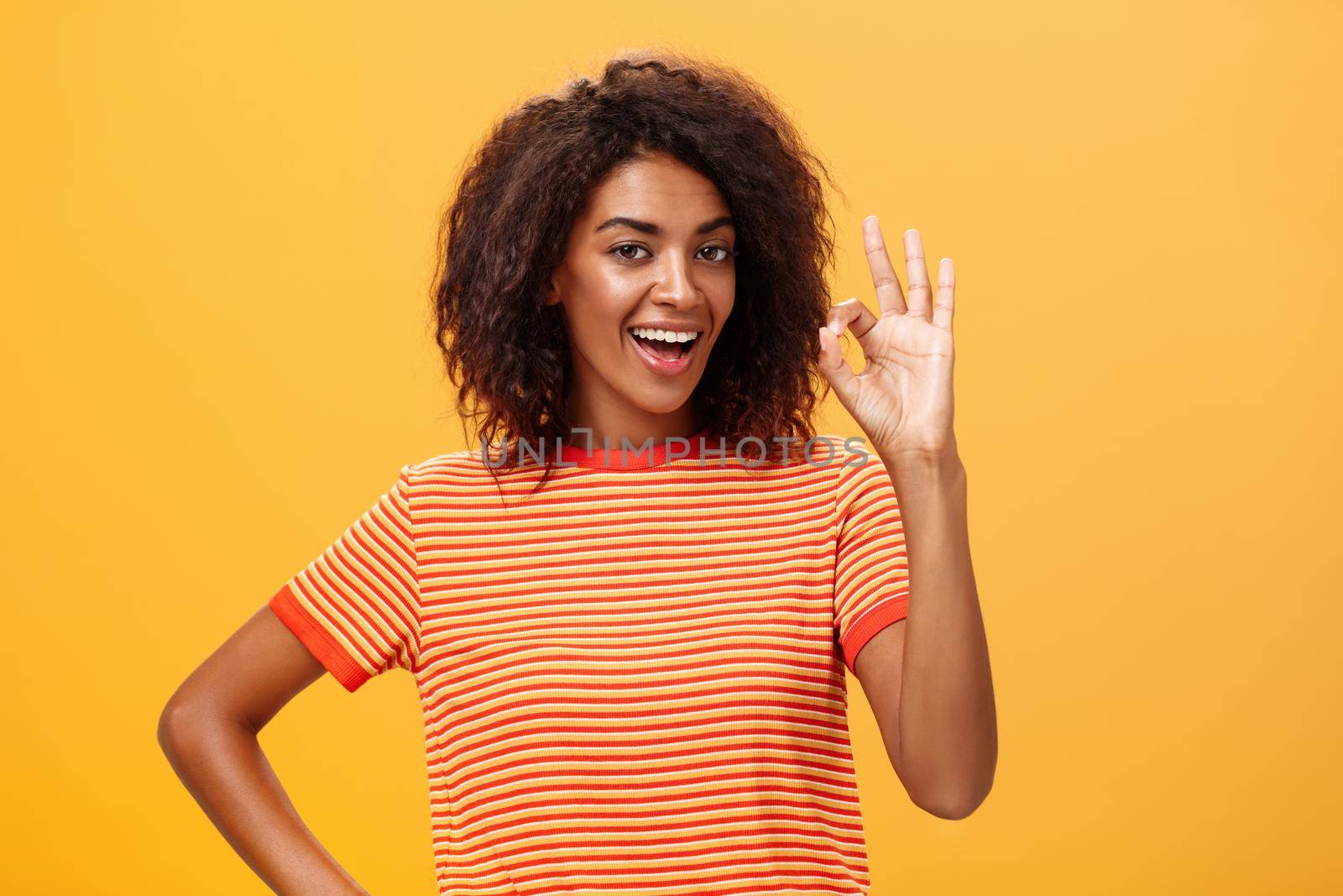 I got it, think it done. Portrait of self-assured good-looking calm and carefree african american woman with curly hairstyle raising ok or excellent gesture and smiling assuring she knows what doing. Body language concept