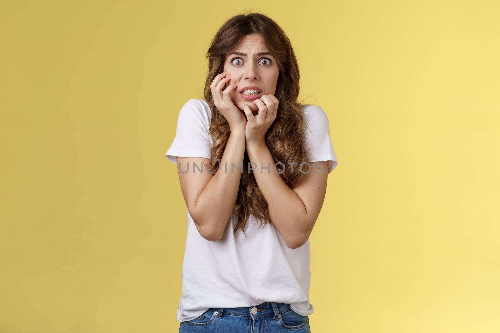 Worried insecure nervous european girl biting fingernails stare camera anxious panic touch cheek timid intense stooping stand yellow background scared terrified consequences someone found up secret. Lifestyle.