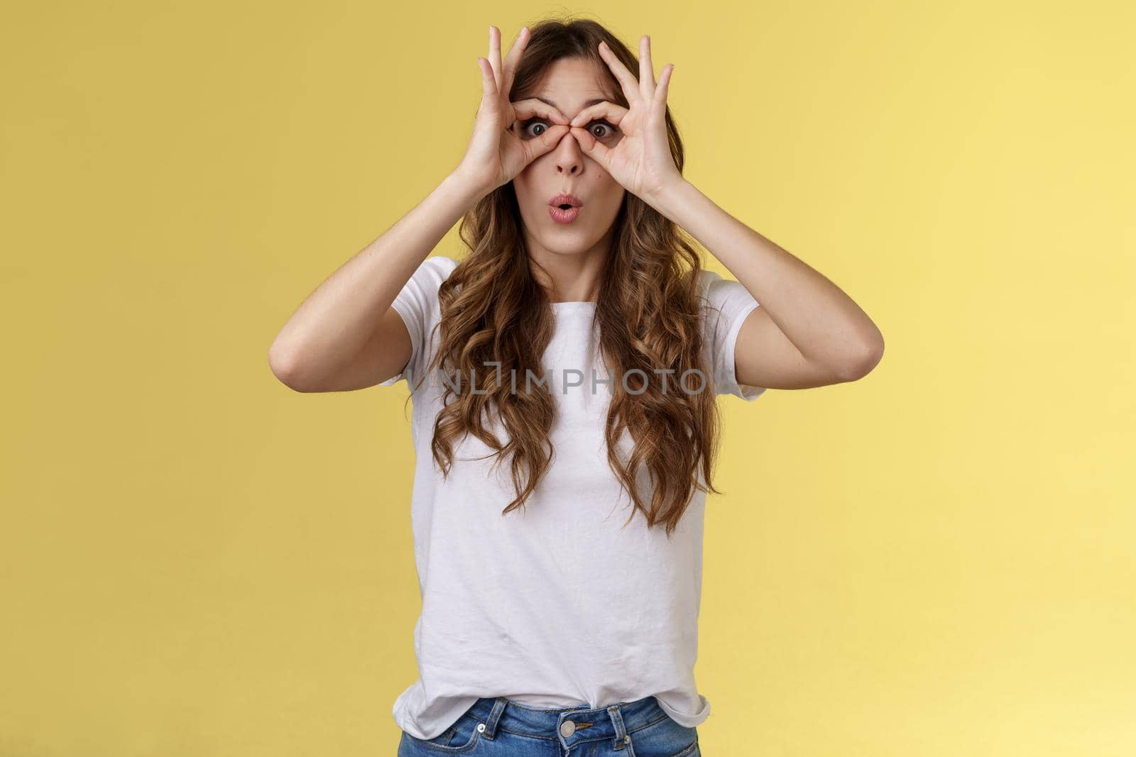 Wow so cool. Girl obersve interesting awesome event show okay perfection gesture look through ring hands folding lips amused wondered glance camera fascinated admiration interested yellow background.