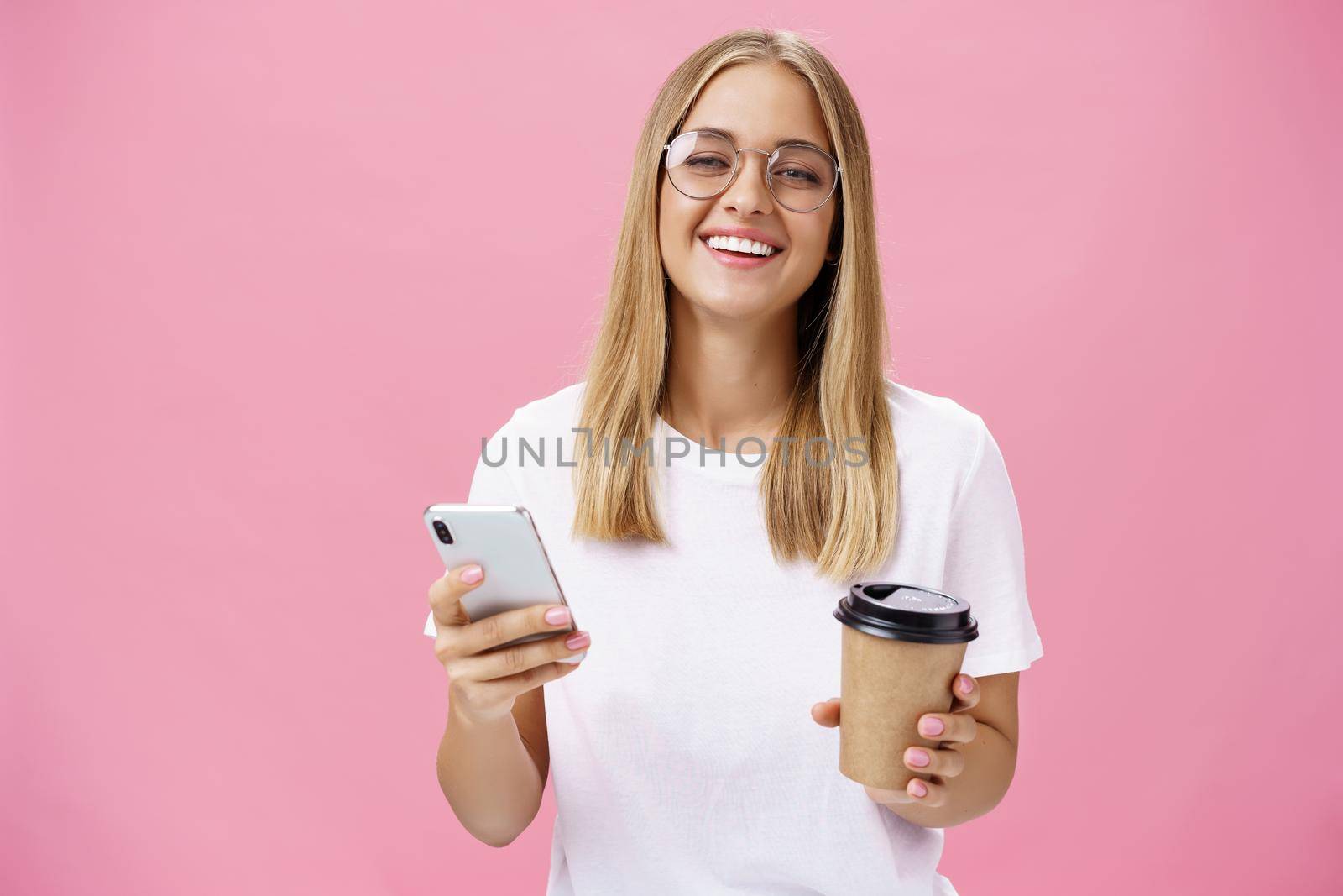 Busy freelancer sipping coffee and working via smartphone talking to clients while sitting in cafe or coworking place, laughing joyfully at camera with broad smile holding paper cup and cellphone. Van life, lifestyle, technology and digital nomad concept
