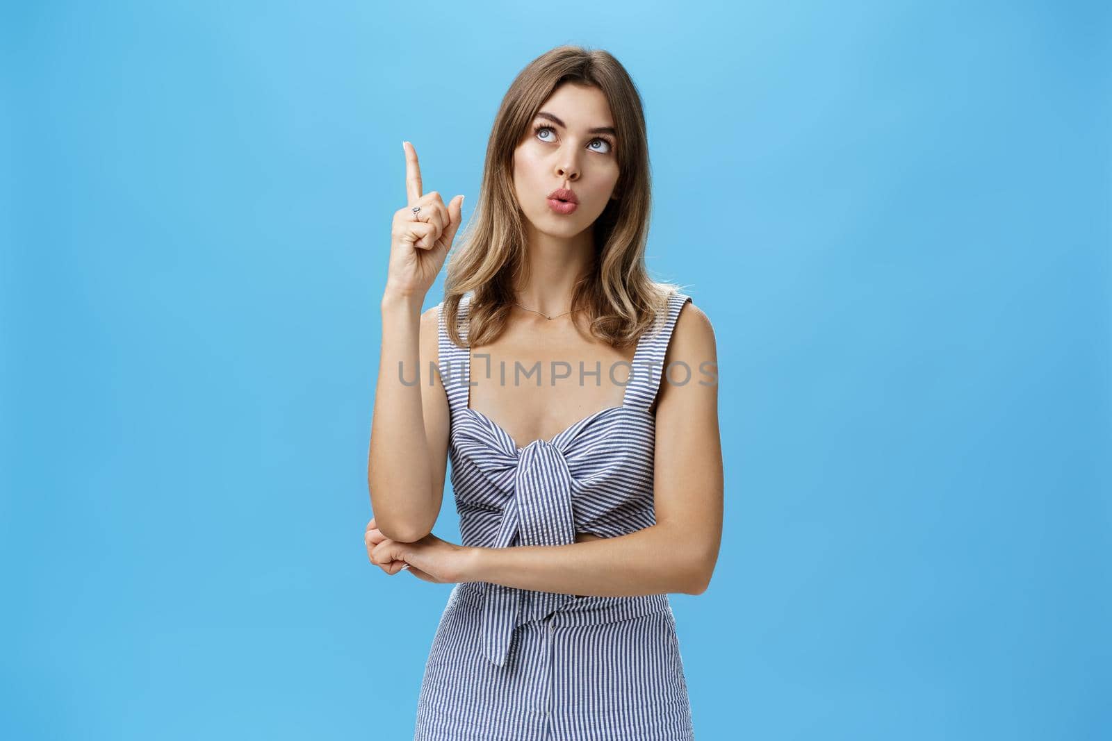 Portrait of beautiful creative cute adult woman daydreaming or thinking looking up with thoughtful expression trying think, raising index finger in eureka gesture standing upright like A-student.